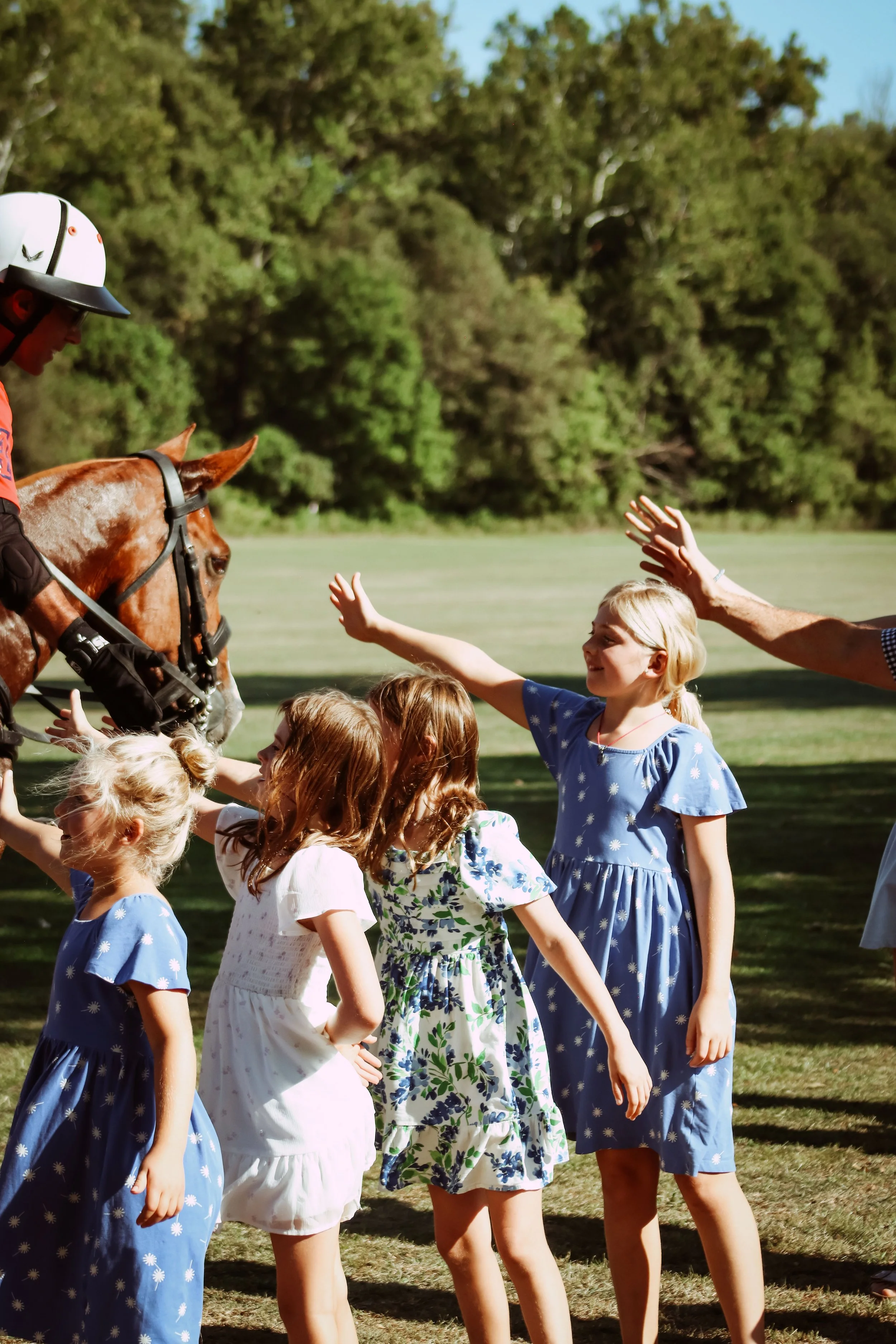 Several children attending the 2025 Charity Polo Cup greet a polo player and their horse.