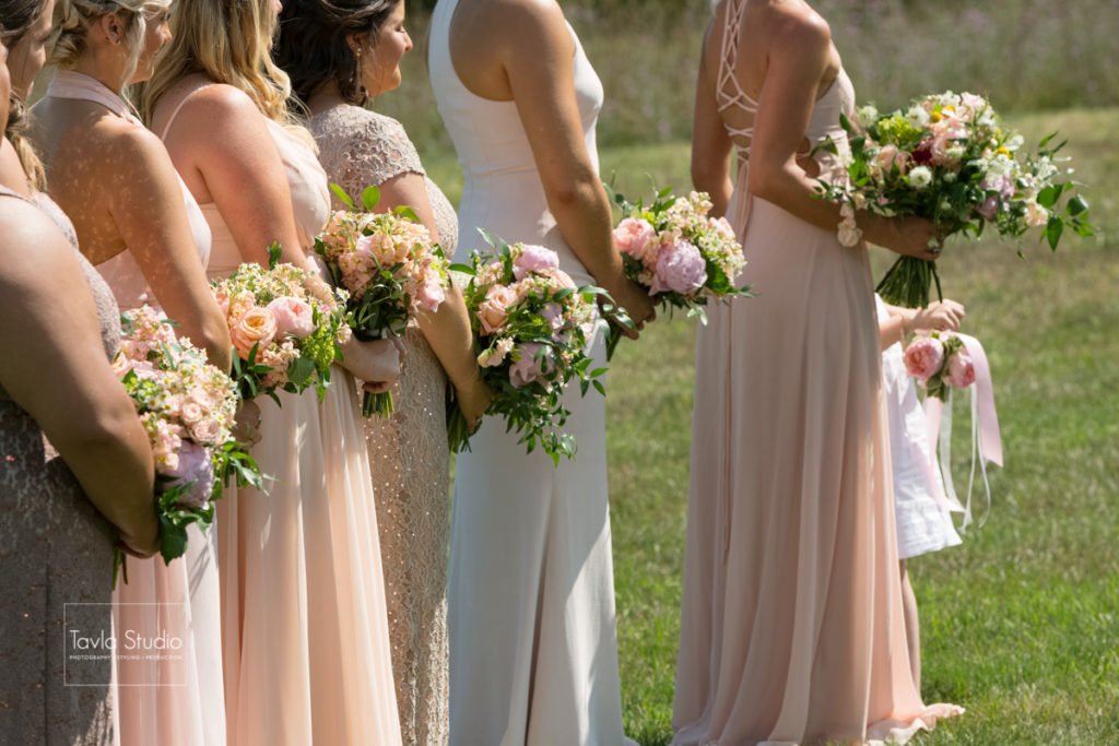 Bridesmaids in pastel dresses holding bouquets at an outdoor wedding ceremony.