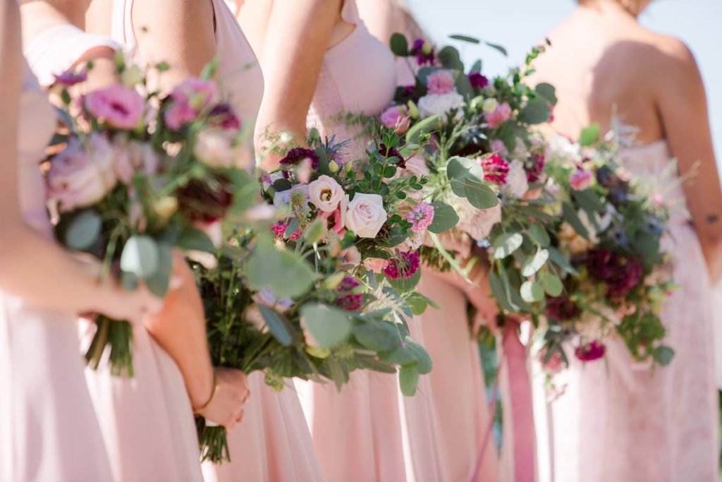 Bridesmaids in pink dresses holding bouquets of pink and white flowers with greenery.