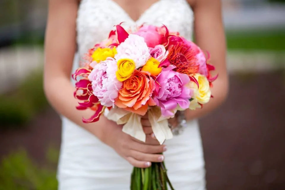 Bride holding colorful bouquet with pink, orange, and yellow flowers.