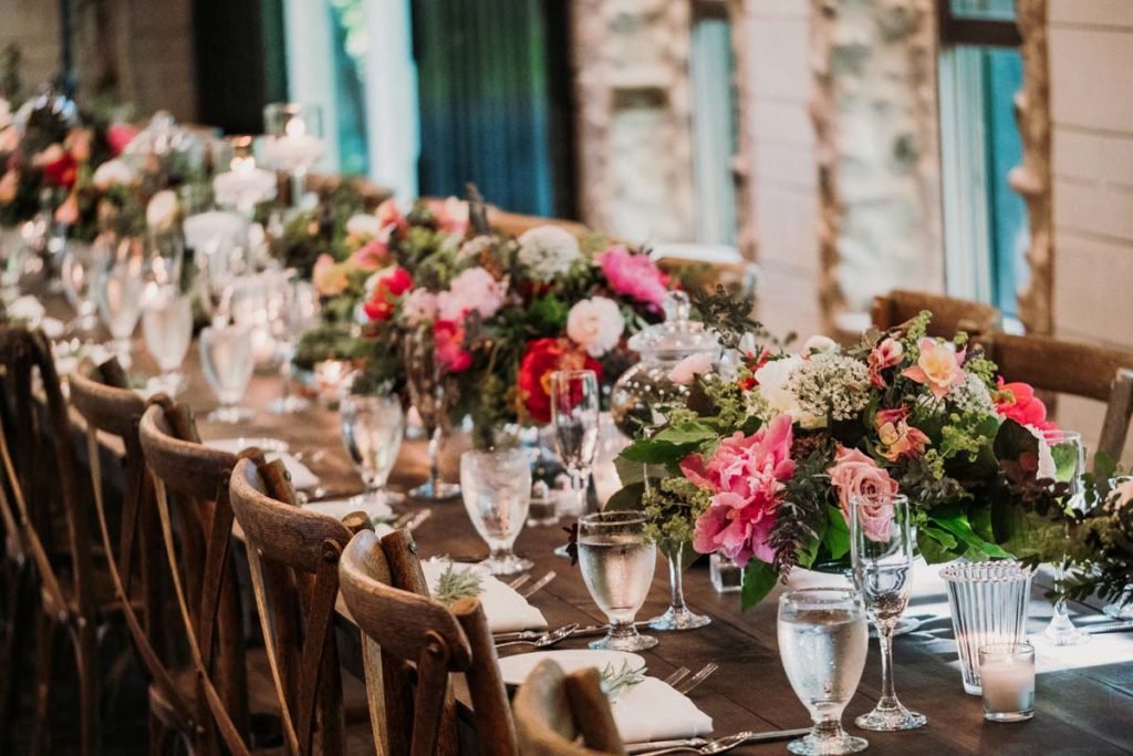 Elegant banquet table setup with wooden chairs, floral centerpieces, glassware, and candles.