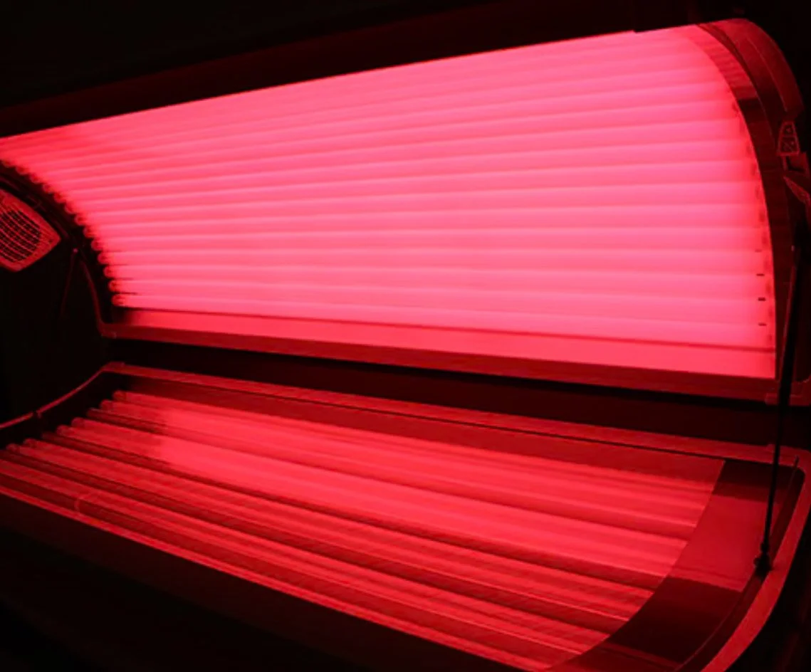 A closed red tanning bed with bright pink light tubes inside.