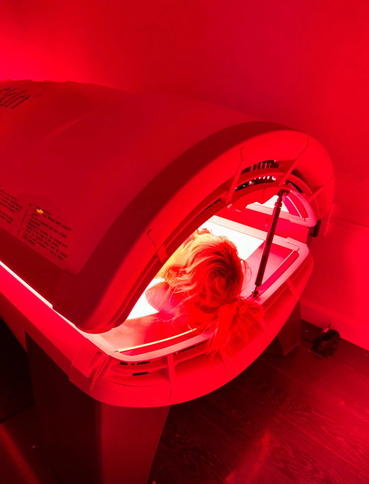 A person lying on a table inside a red-toned tanning bed, undergoing UV light tanning.