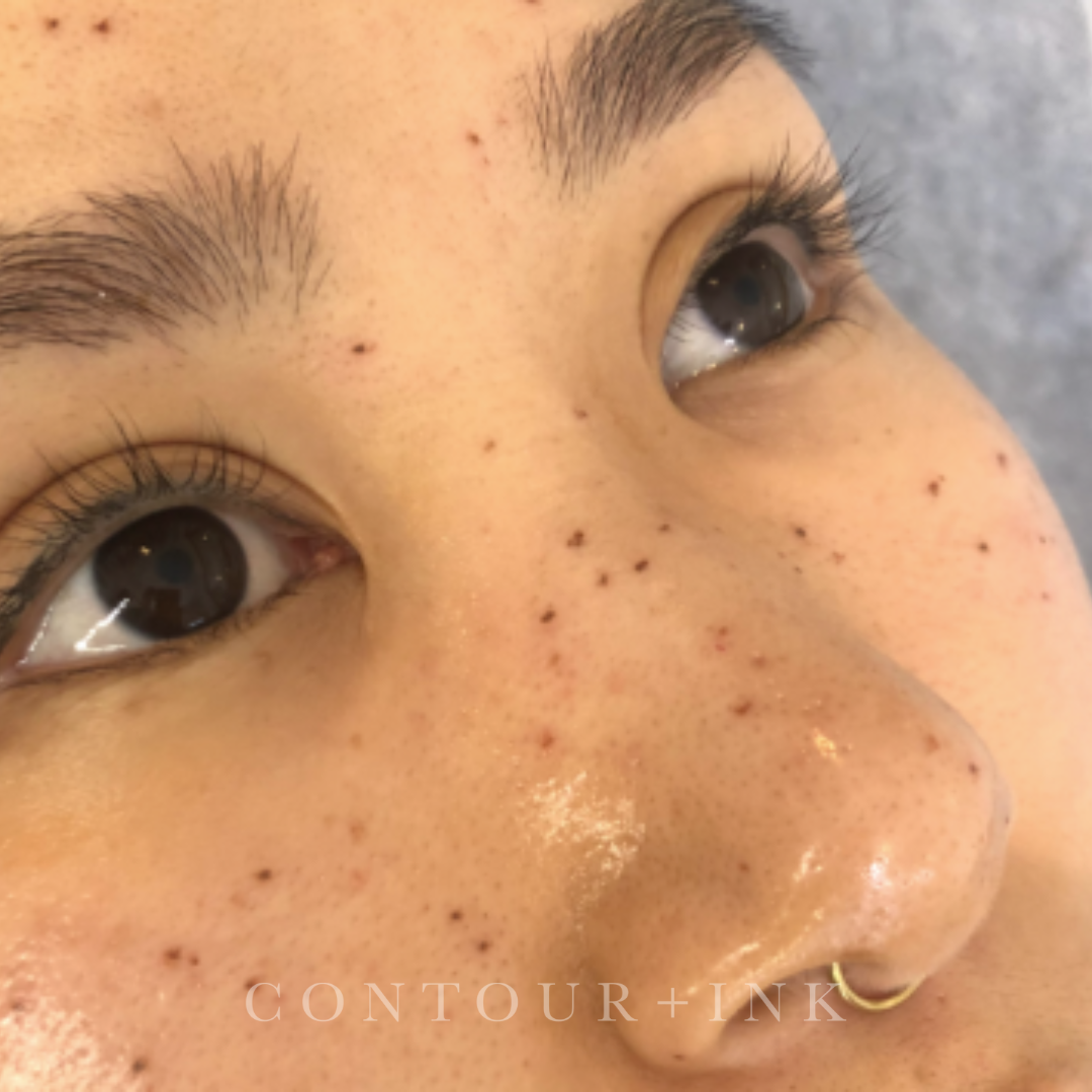Close-up of a person's face showing eyes, nose, and freckles, with makeup and a small gold hoop earring.