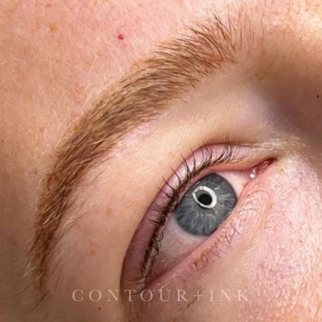Close-up image of a person's eye, showing gray iris, eyelashes, and eyebrow, with skin details including a small blemish and fine hair.
