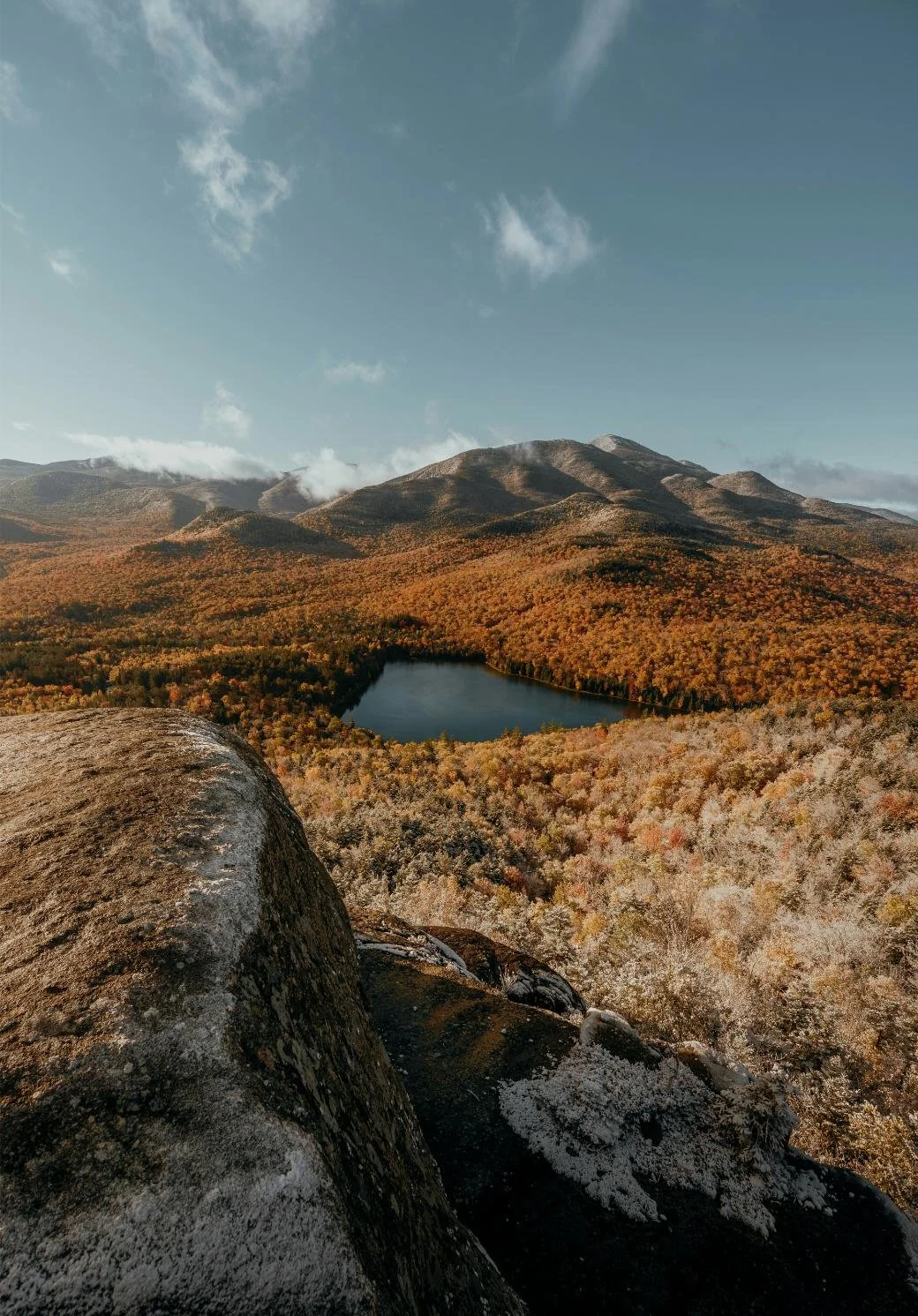 Mountain landscape with autumn foliage, rock in foreground, and lake.