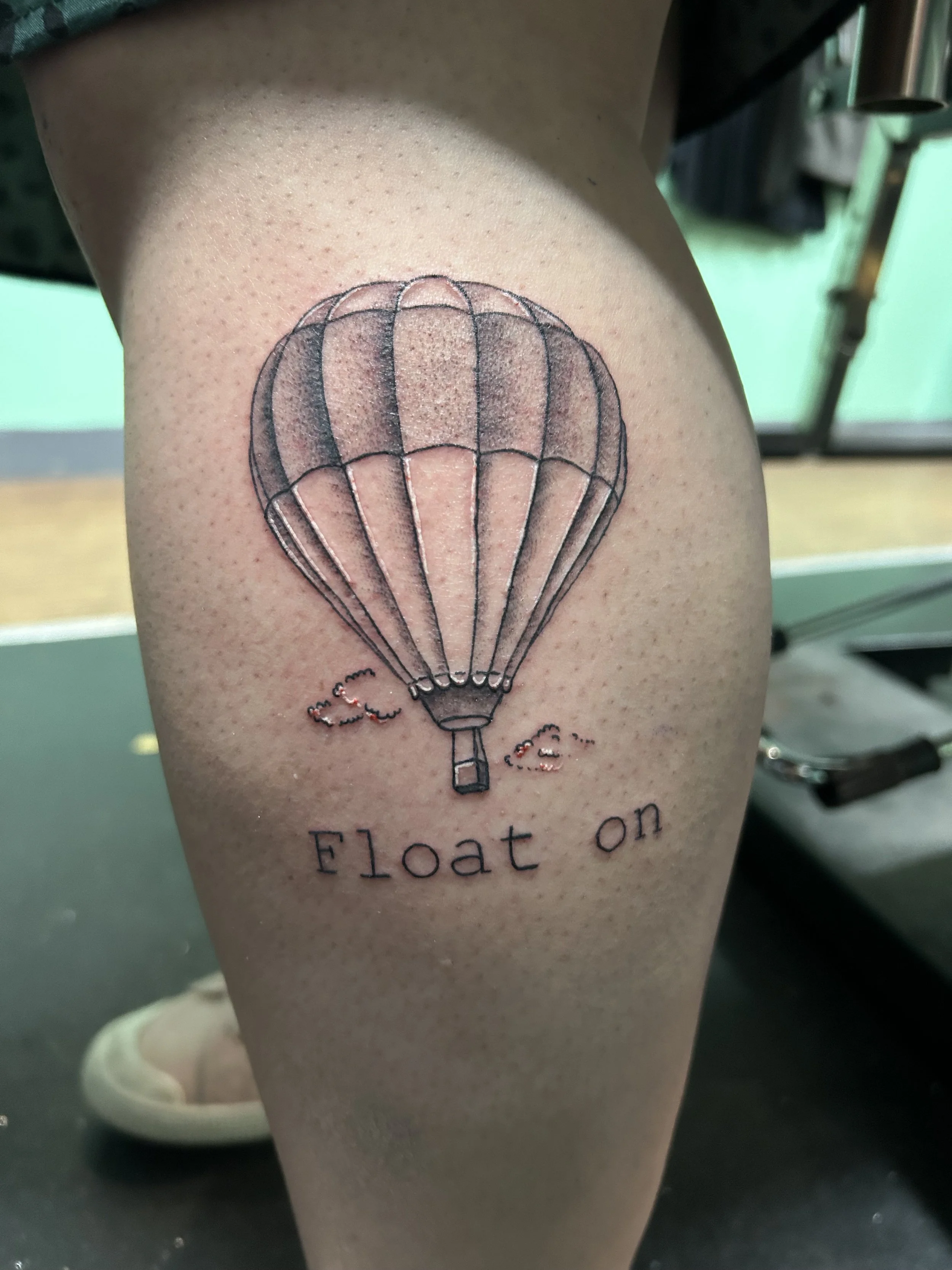Tattoo of a hot air balloon with the text 'Float on' beneath it on a person's upper thigh.