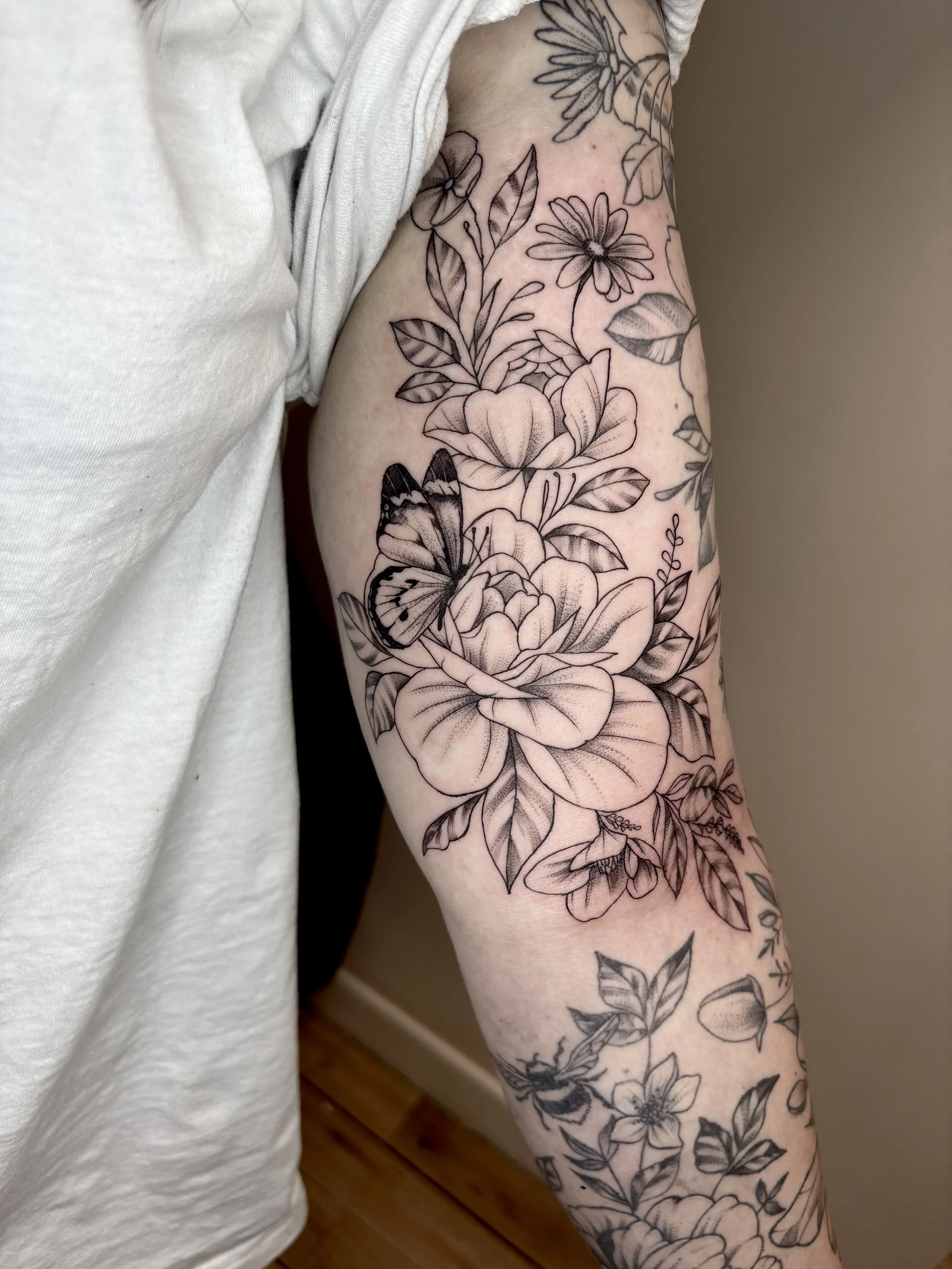 Black and gray floral tattoo with a butterfly on a person's arm.