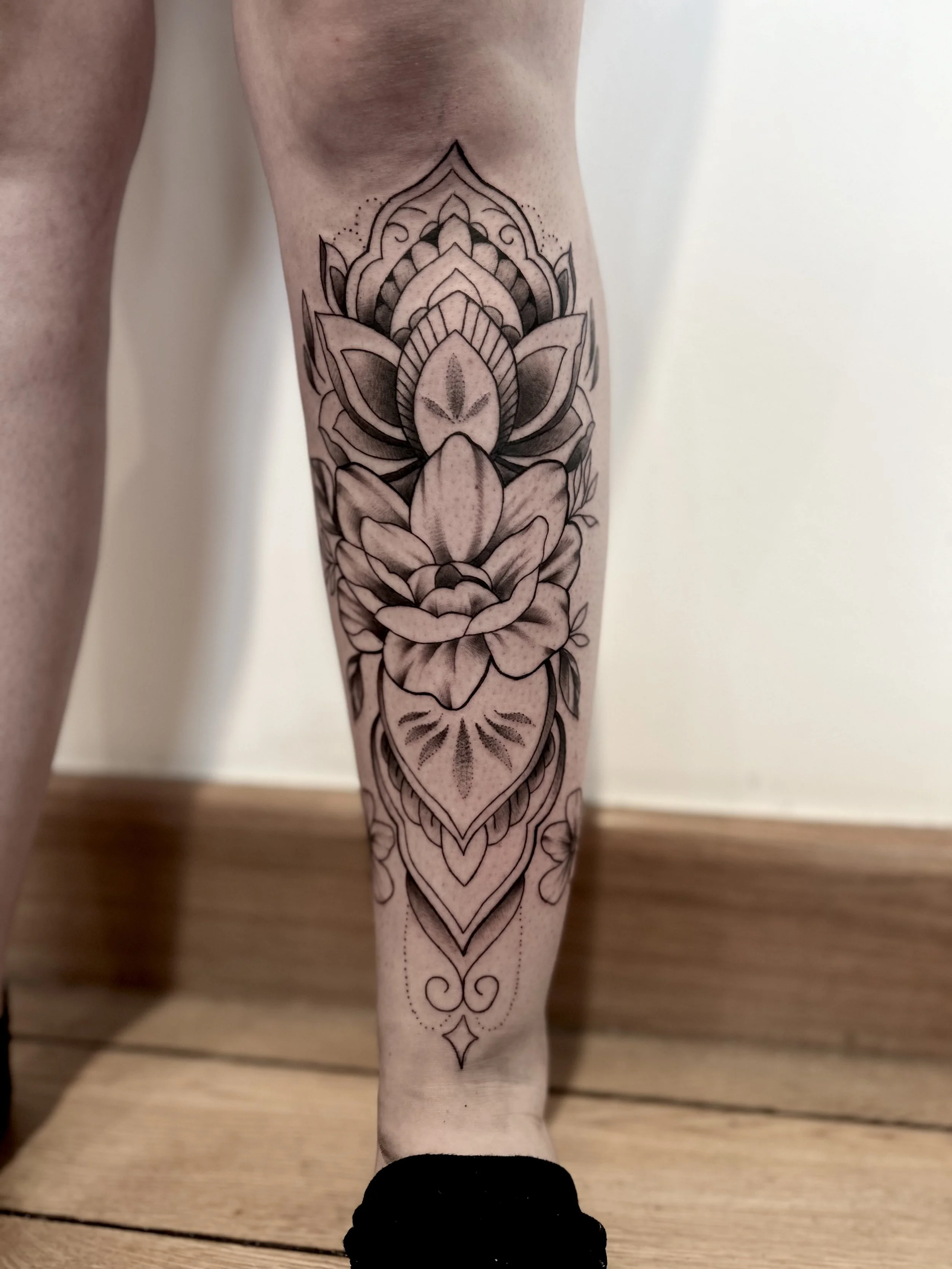 Black and gray tattoo of a detailed lotus flower, leaf motifs, and decorative elements.