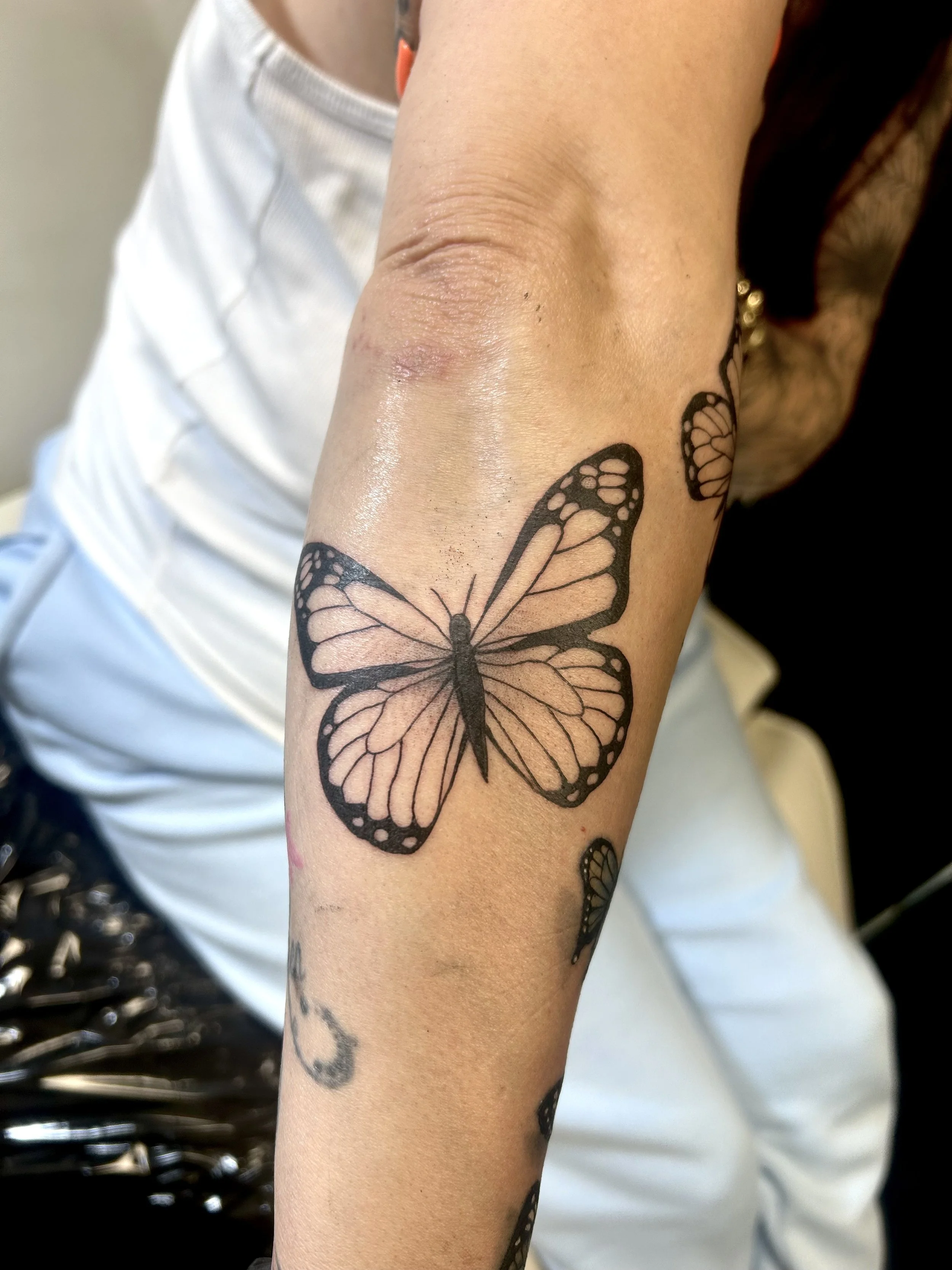 Tattoo of a butterfly on a person's forearm with other smaller butterfly tattoos nearby.