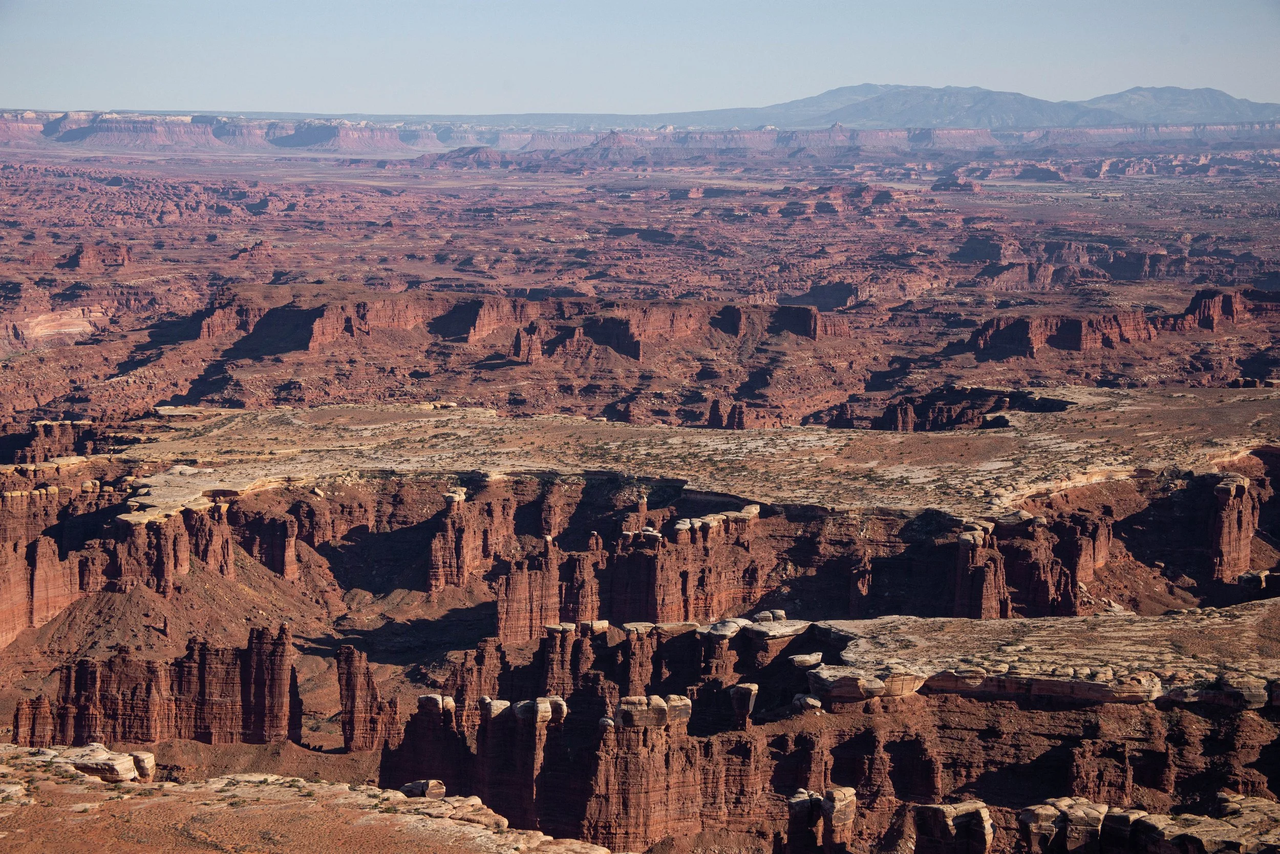 A vast view of the Grand Canyon displaying layered red rock formations, cliffs, and deep valleys under a clear sky.