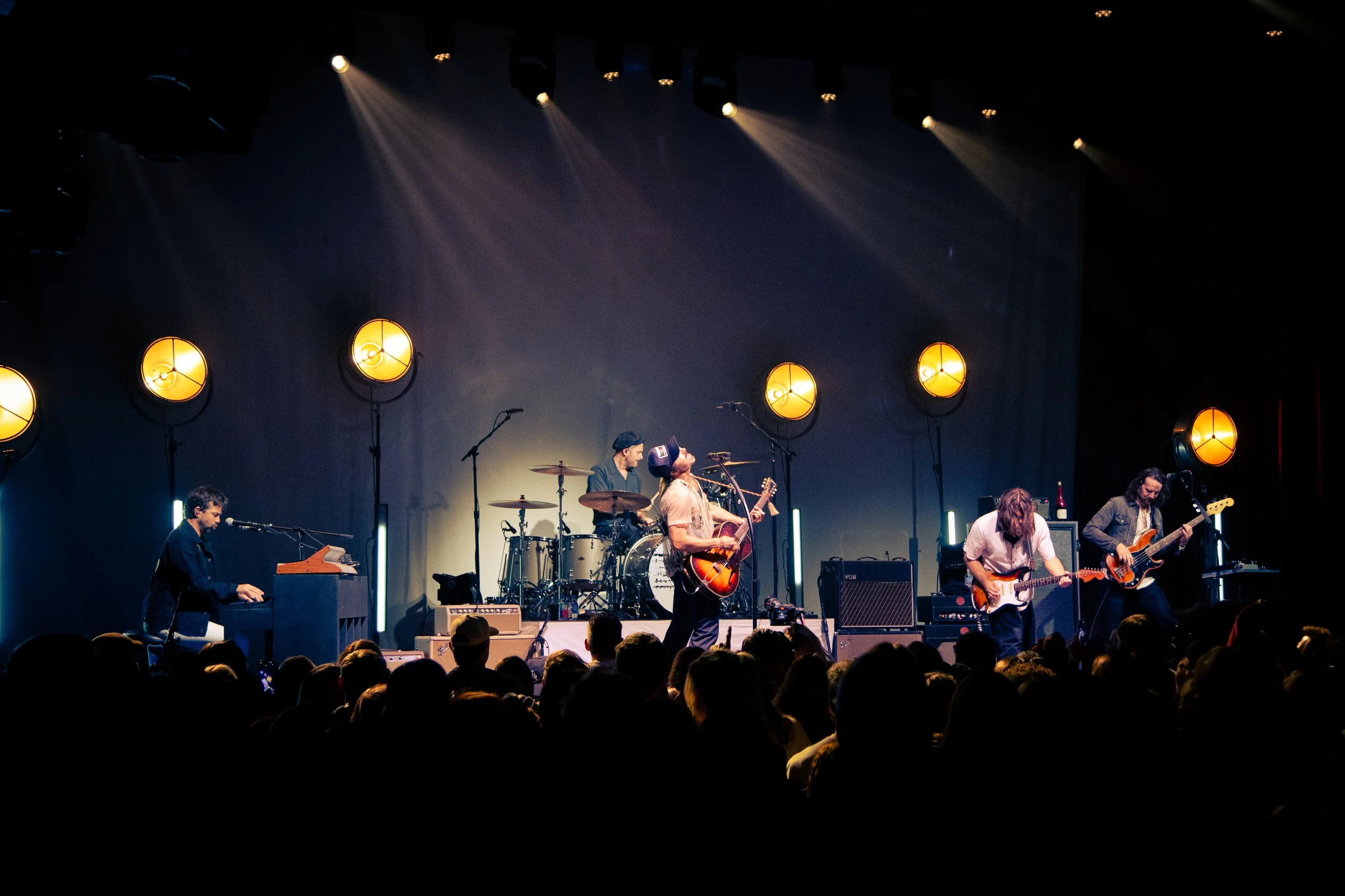 Band performing on stage with yellow circular lights, audience in foreground.