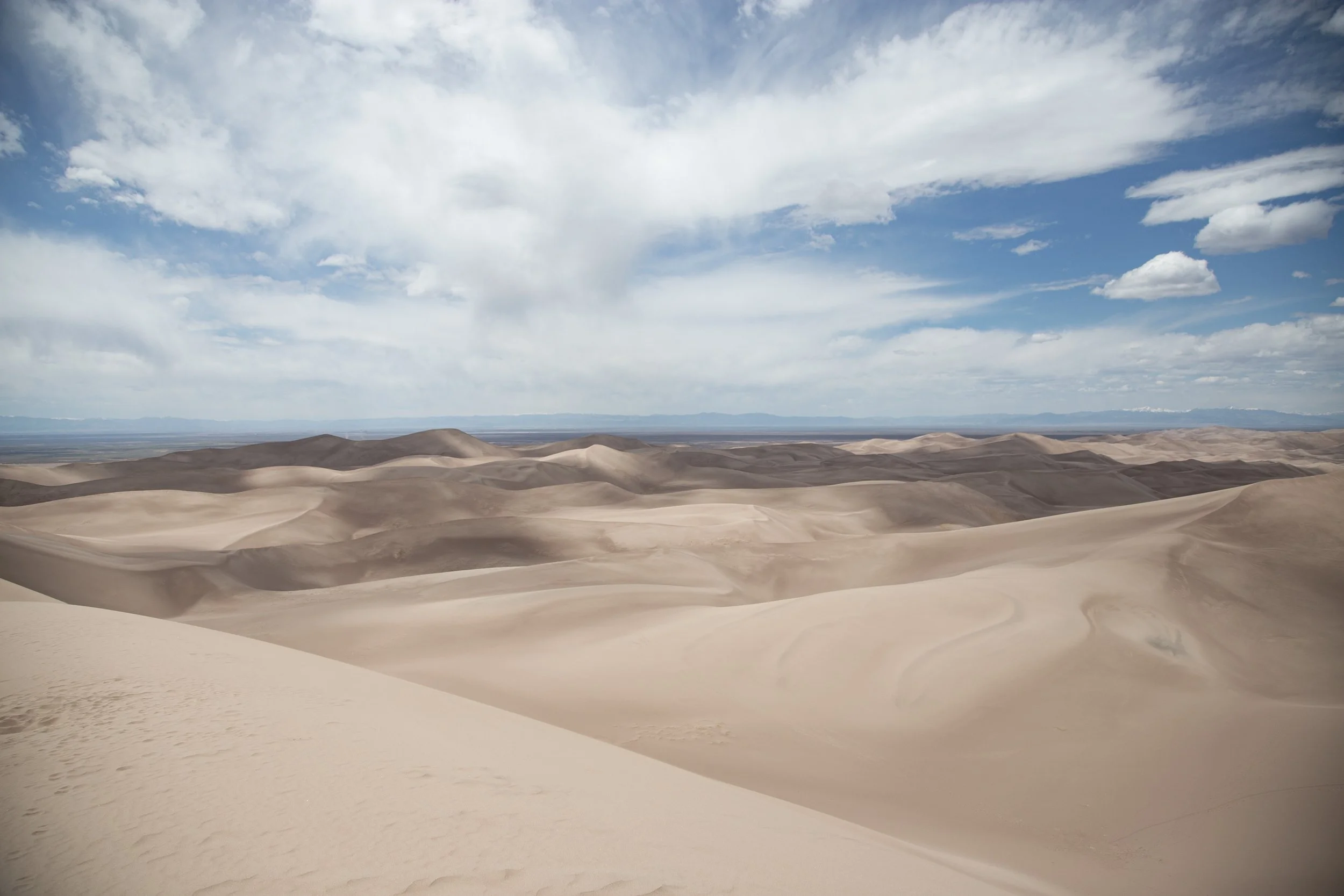 A vast desert landscape with sand dunes under a partly cloudy sky.