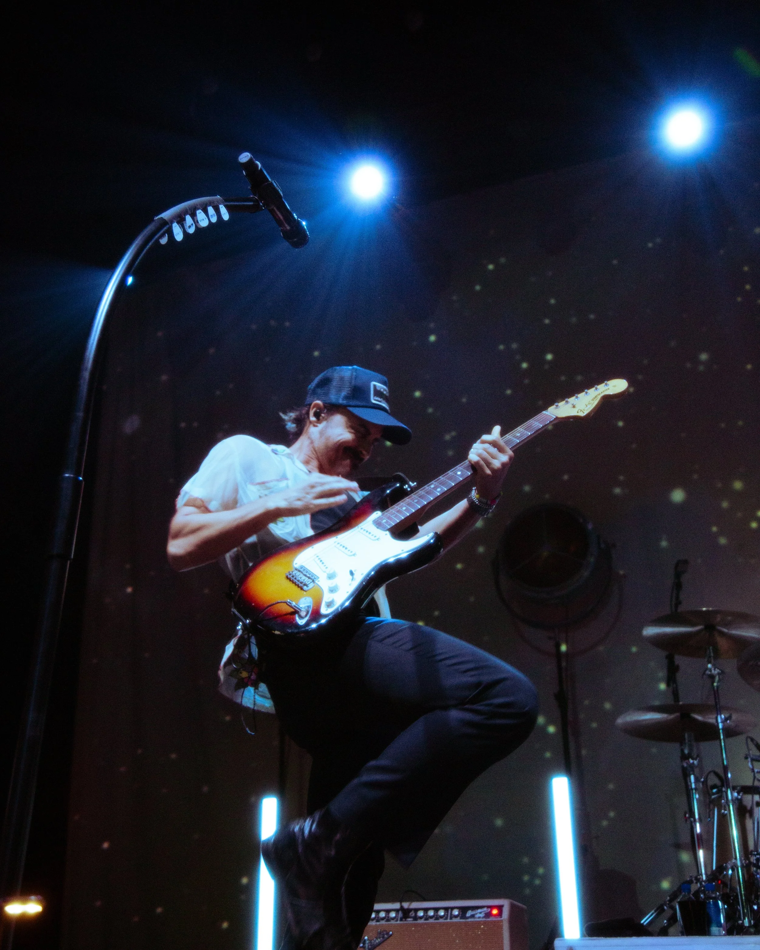 A musician playing an electric guitar on stage with bright blue lights overhead.