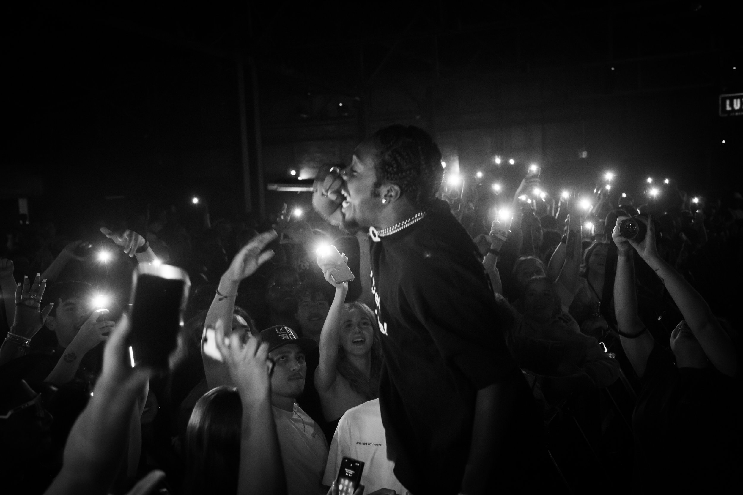 A lively concert scene with a singer performing on stage, surrounded by excited audience members holding up their phones with flashes on, capturing the moment.