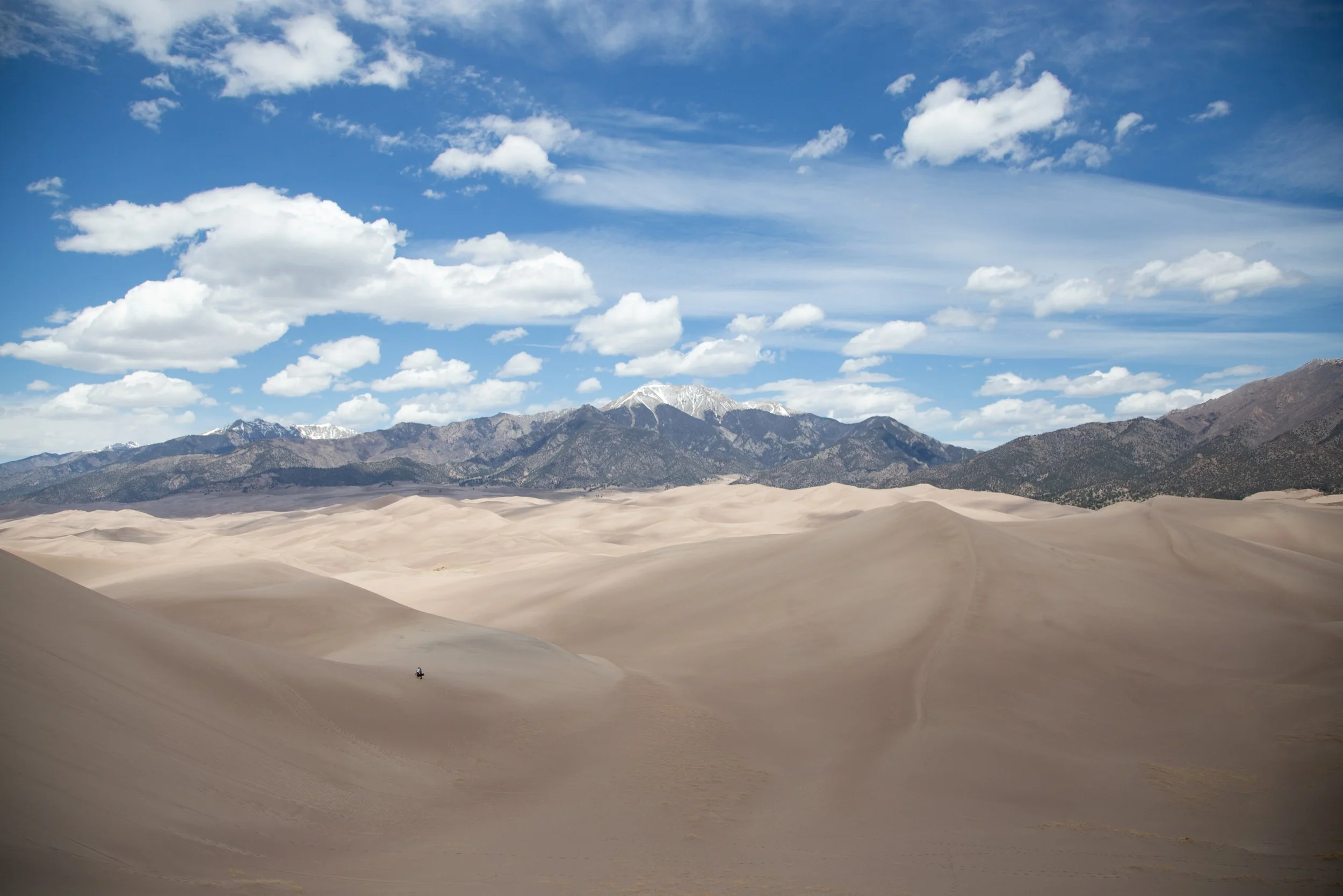 Photos of sand dunes with a mountain range and cloudy sky in the background.