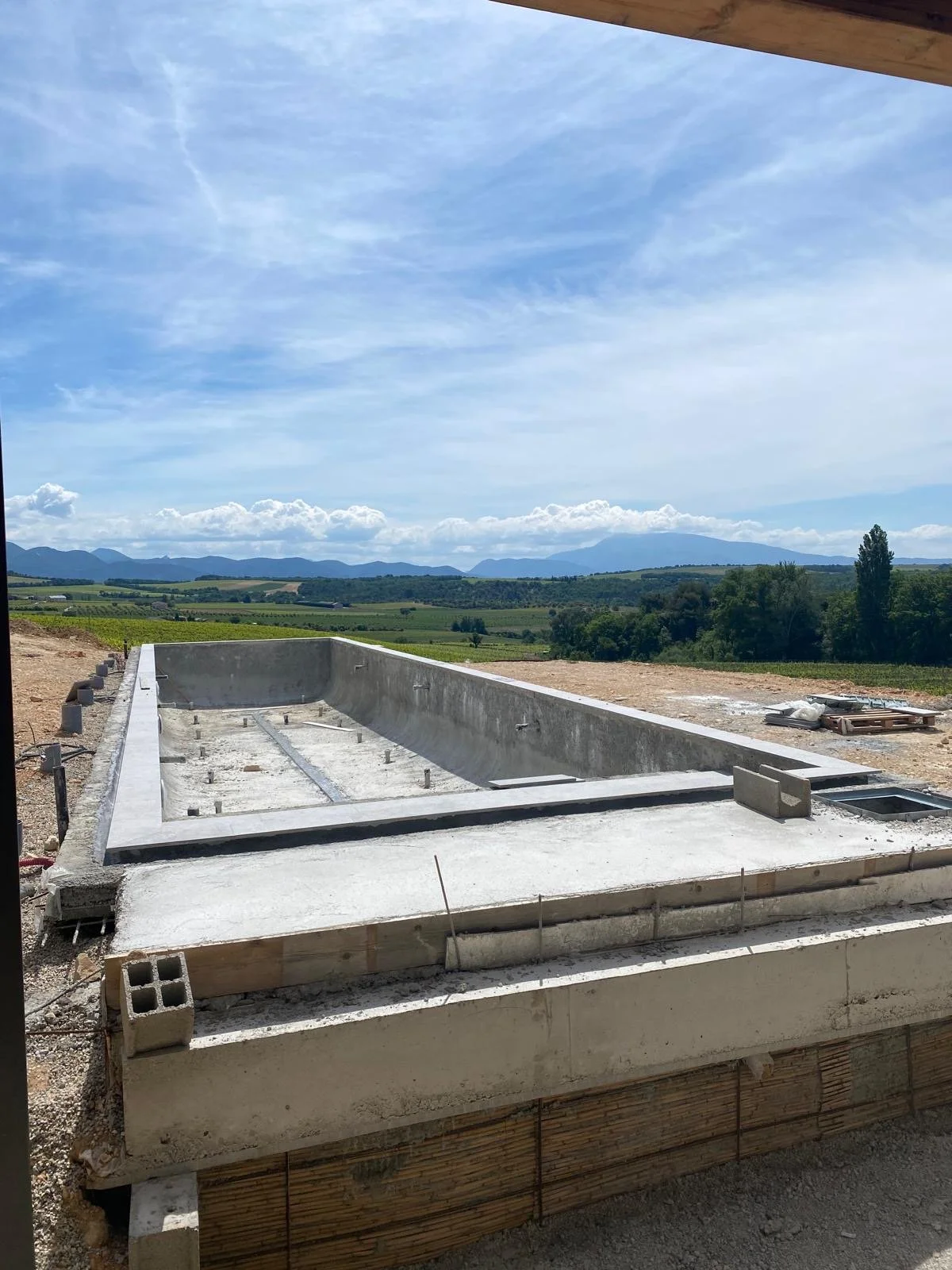 Bouw van een zwembad in een open landschap met bergen op de achtergrond under een blauwe lucht.