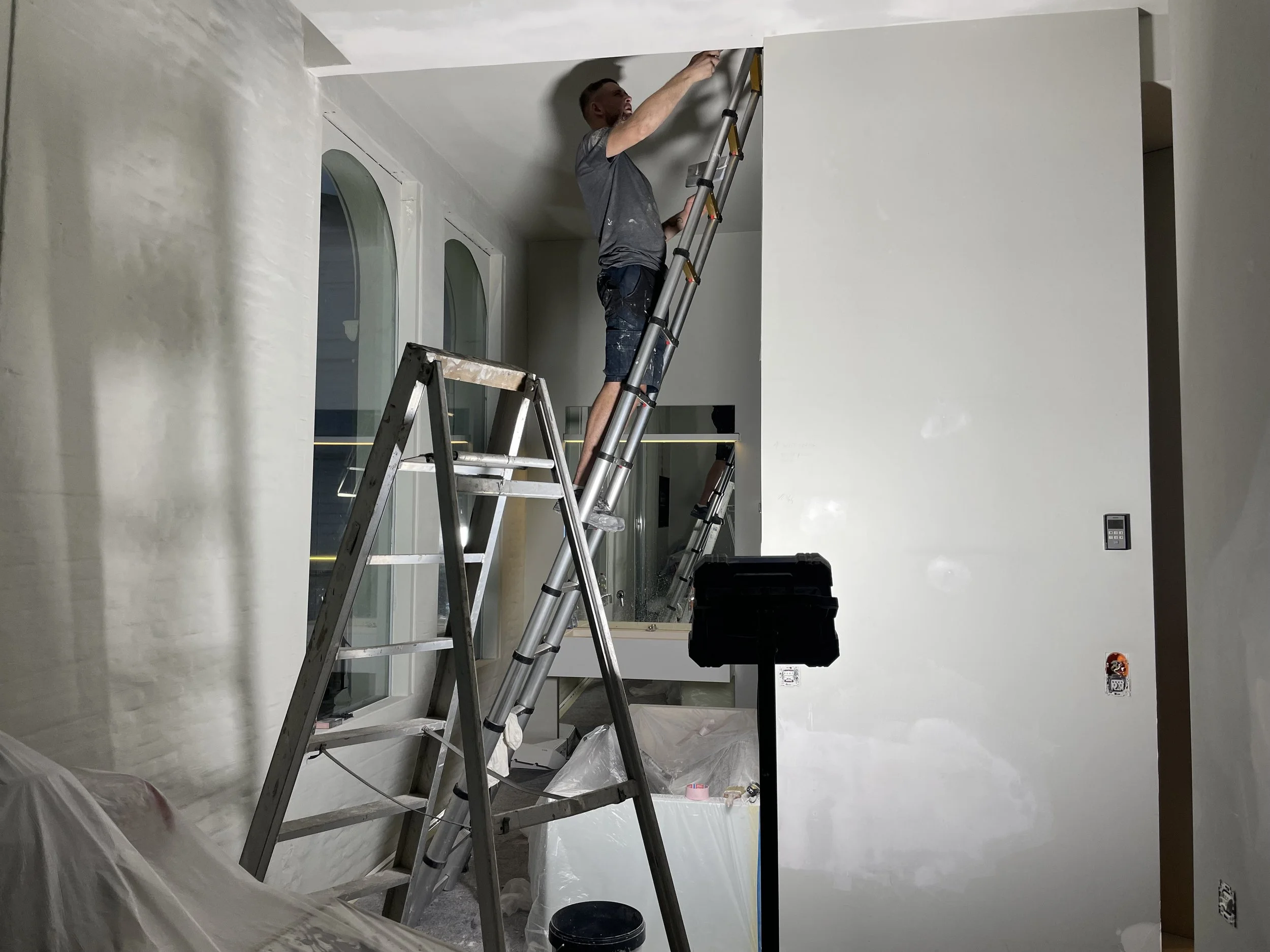 Man op een ladder die verf aan het plafond aanbrengt in een interieurruimte.