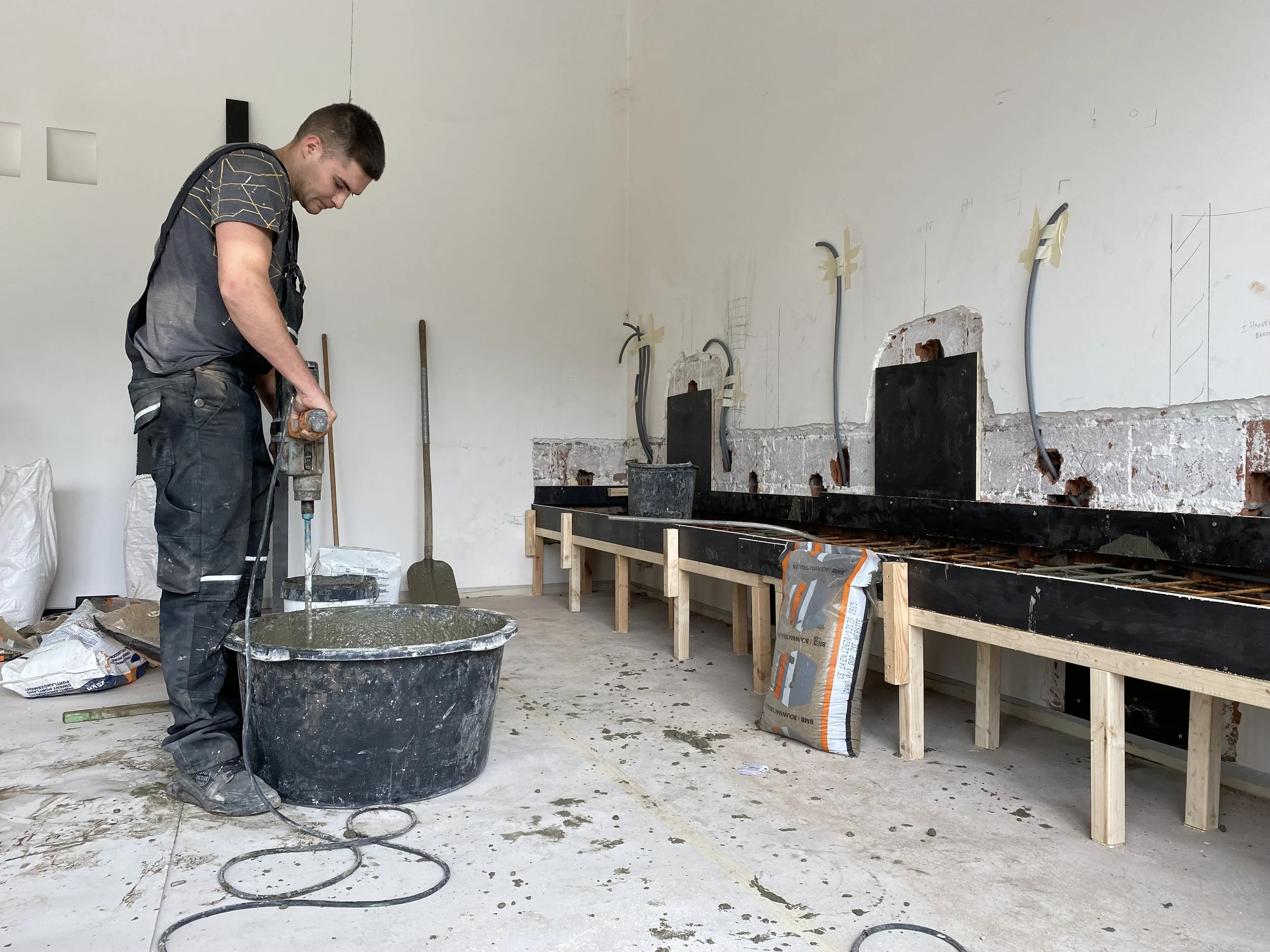 Mann werkt met betonmix in een bouwruimte met lift en muurproject. 