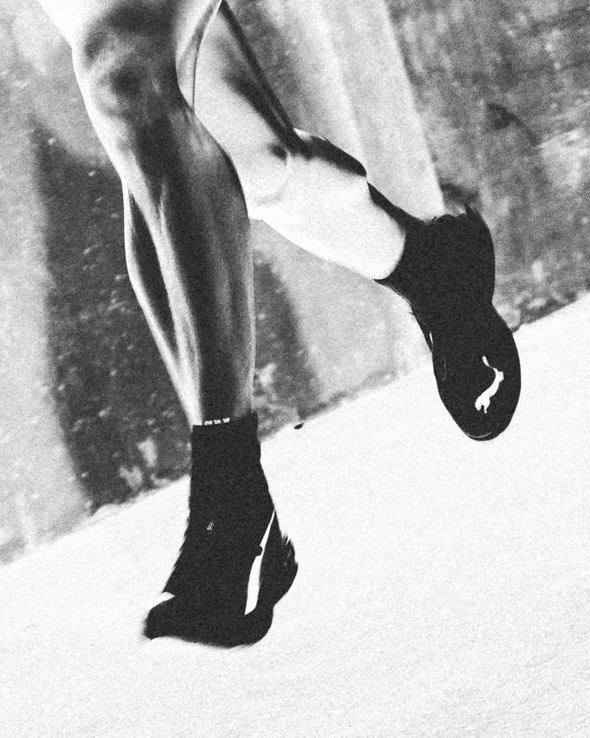 Black and white photo of a person skateboarding on a paved surface outdoors, wearing a beanie and casual clothing.