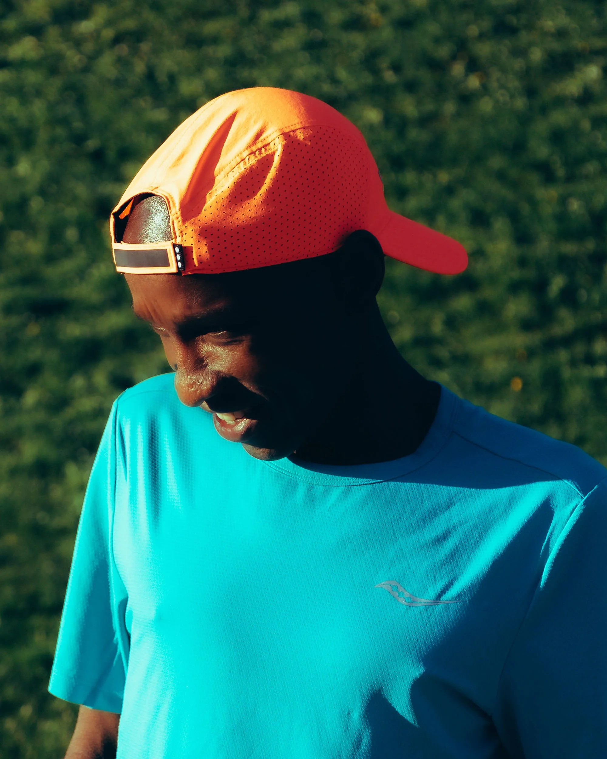 A person wearing an orange baseball cap and a blue athletic shirt outdoors on a sunny day.