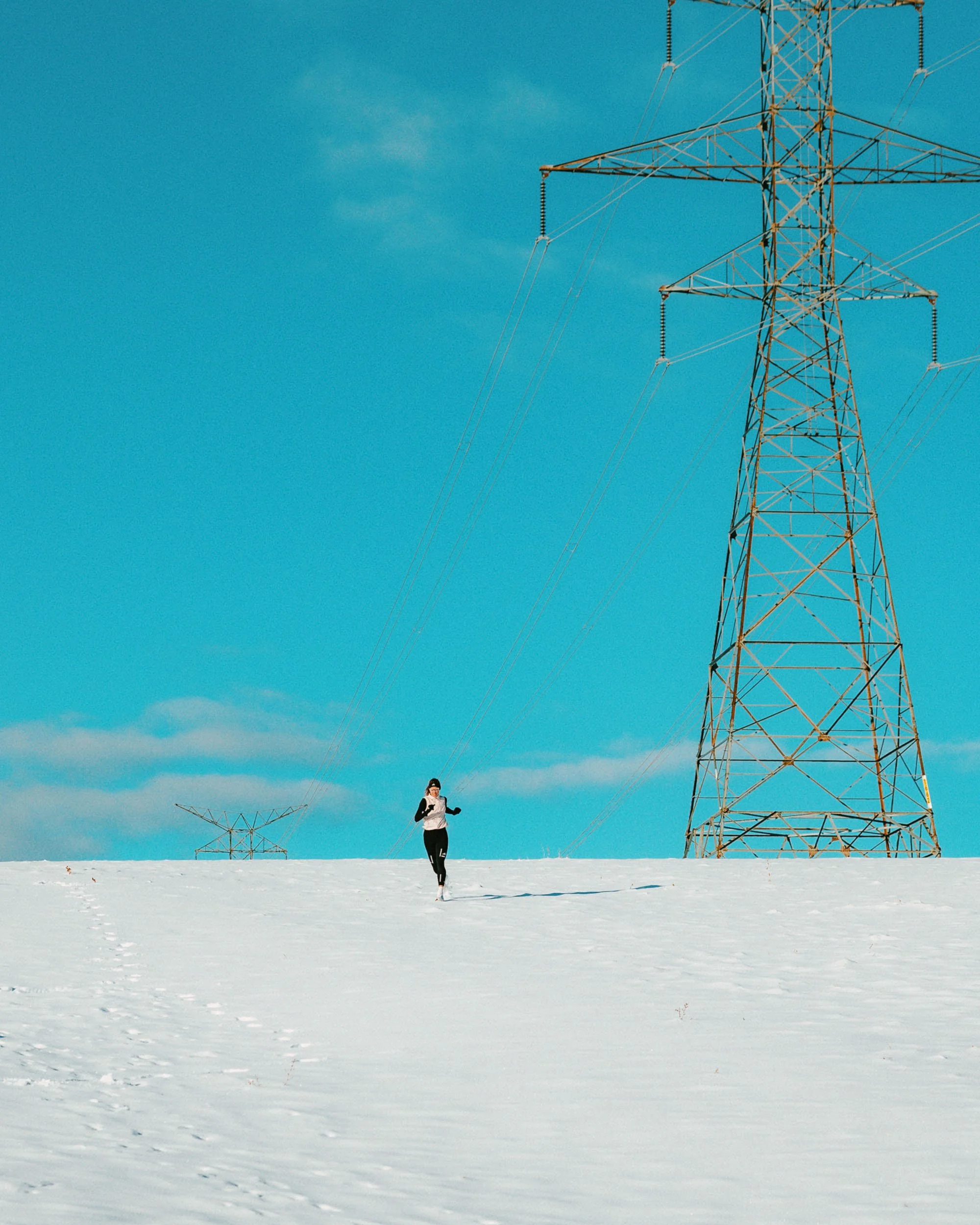 A person running in the snow near electrical transmission towers under a blue sky.