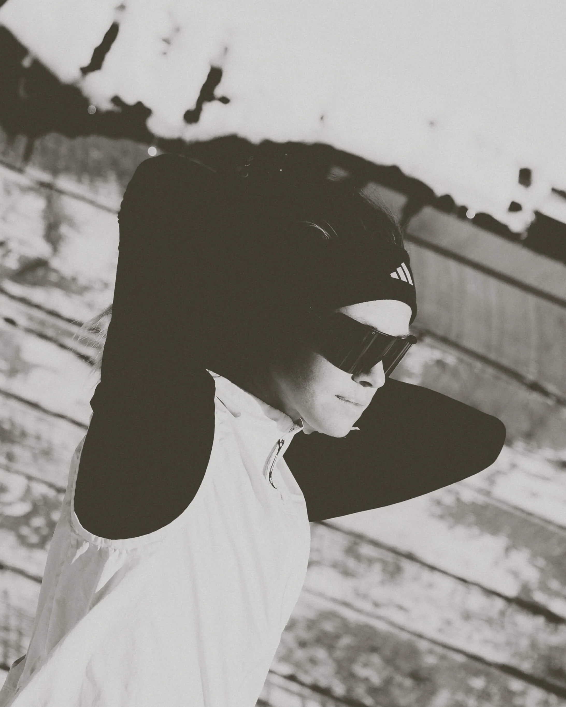 Black and white photo of a person in winter gear, including ski goggles, a headband, and a jacket, sitting outdoors in a snowy landscape.