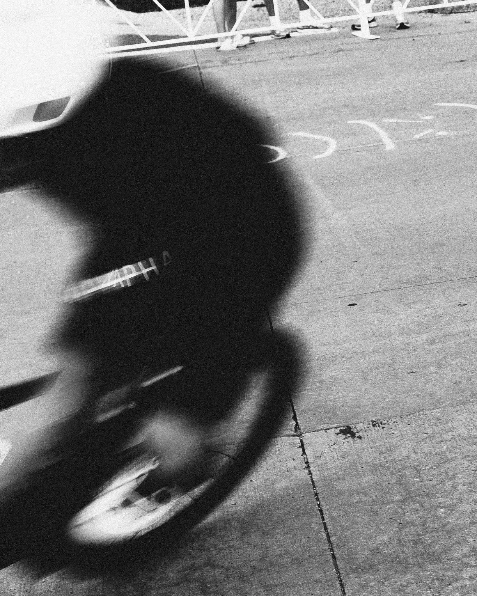 Black and white photo of a skateboard park with a skateboard ramp and in-ground markings of a skating figure. Part of a vehicle is visible in the foreground.