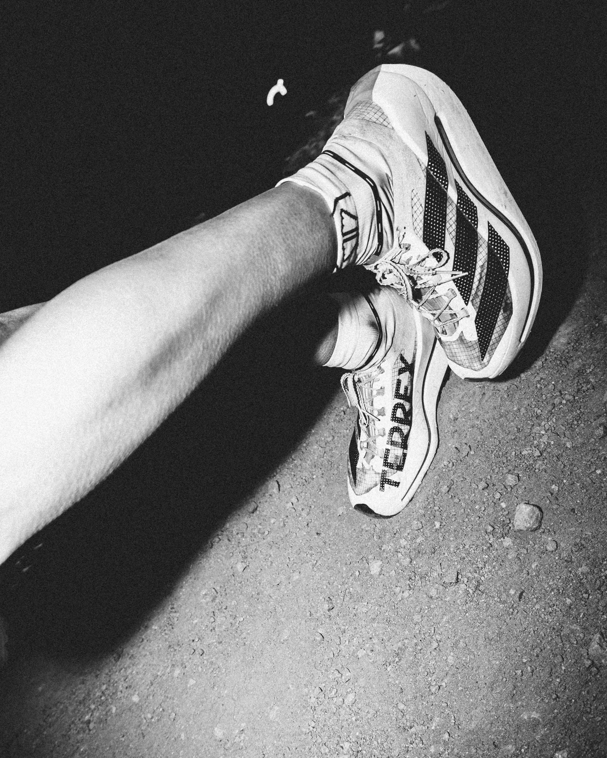 A person's leg wearing a sneaker resting on rough pavement ground, with a small floating object in the background.