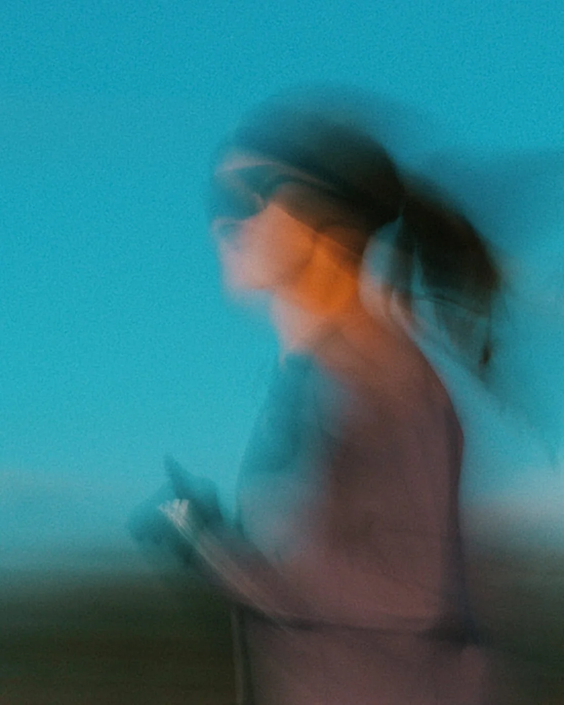 Blurred image of a woman with dark hair tied back, wearing glasses, looking at her phone, against a blue sky background.