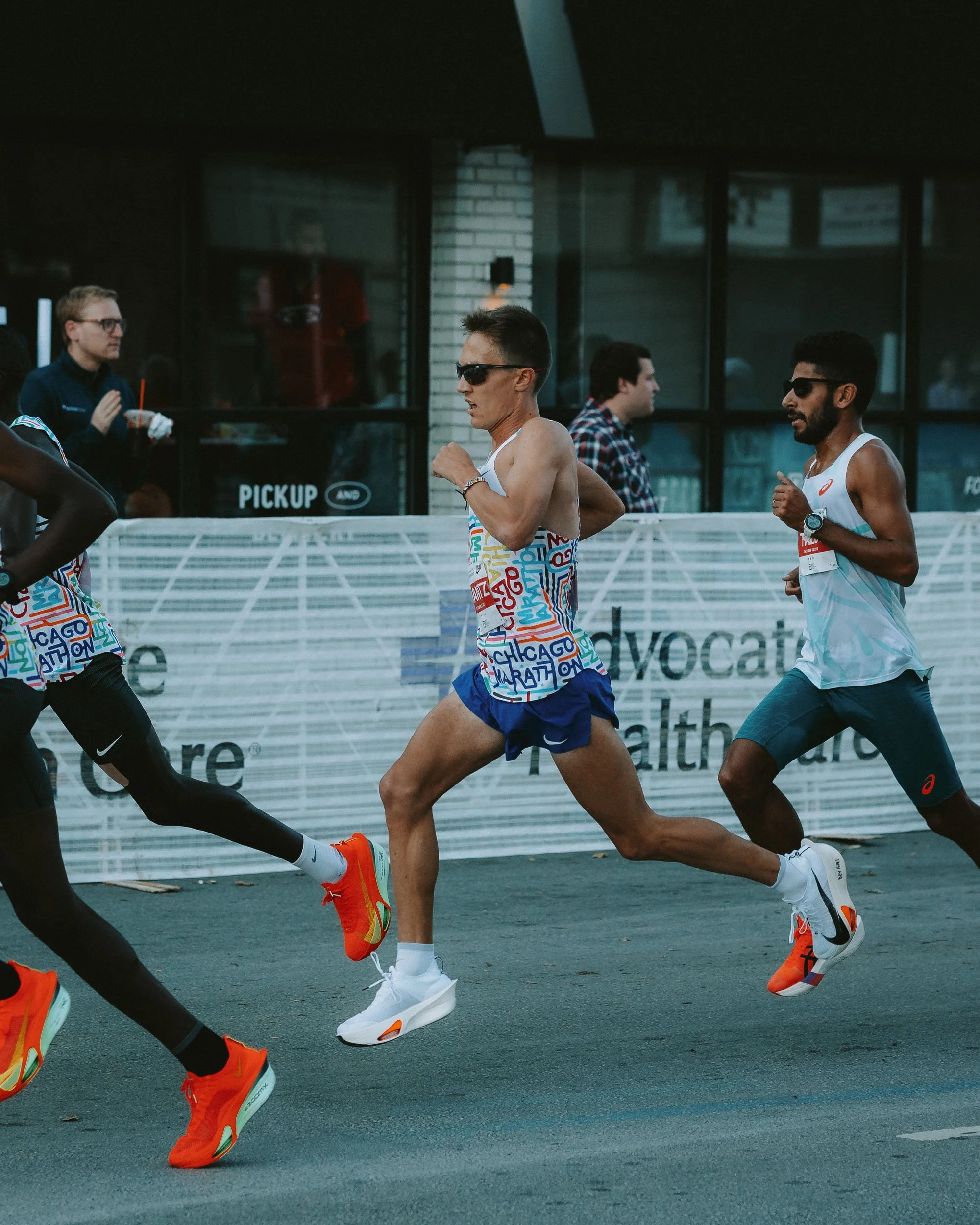 Marathon runners wearing colorful athletic clothing and sunglasses running on the street during a race.