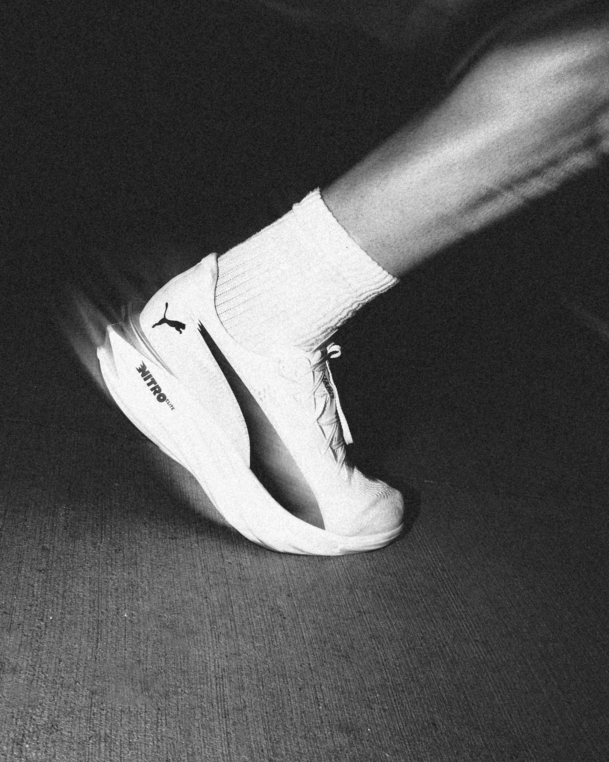 Close-up of a person wearing white athletic shoes and white socks, standing on a textured dark surface.