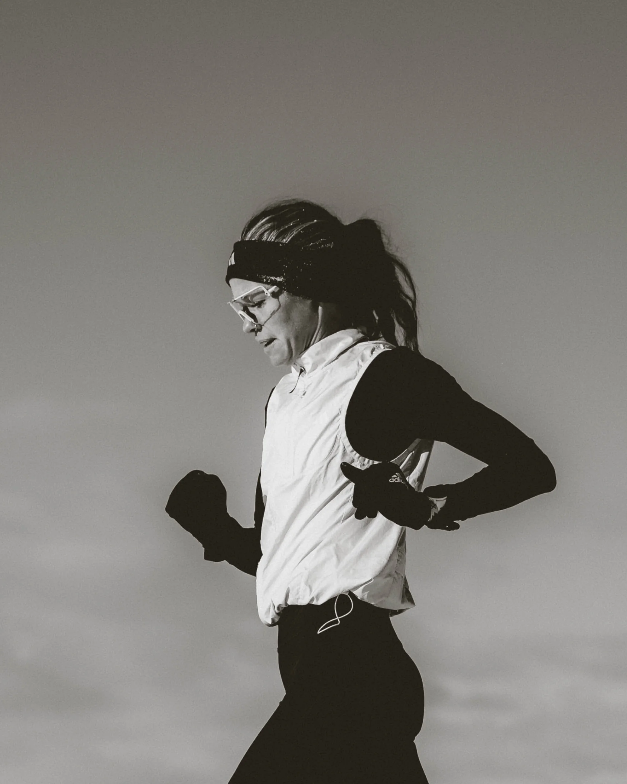 Black and white photo of a woman in athletic gear, running with earbuds, wearing glasses and a headband.