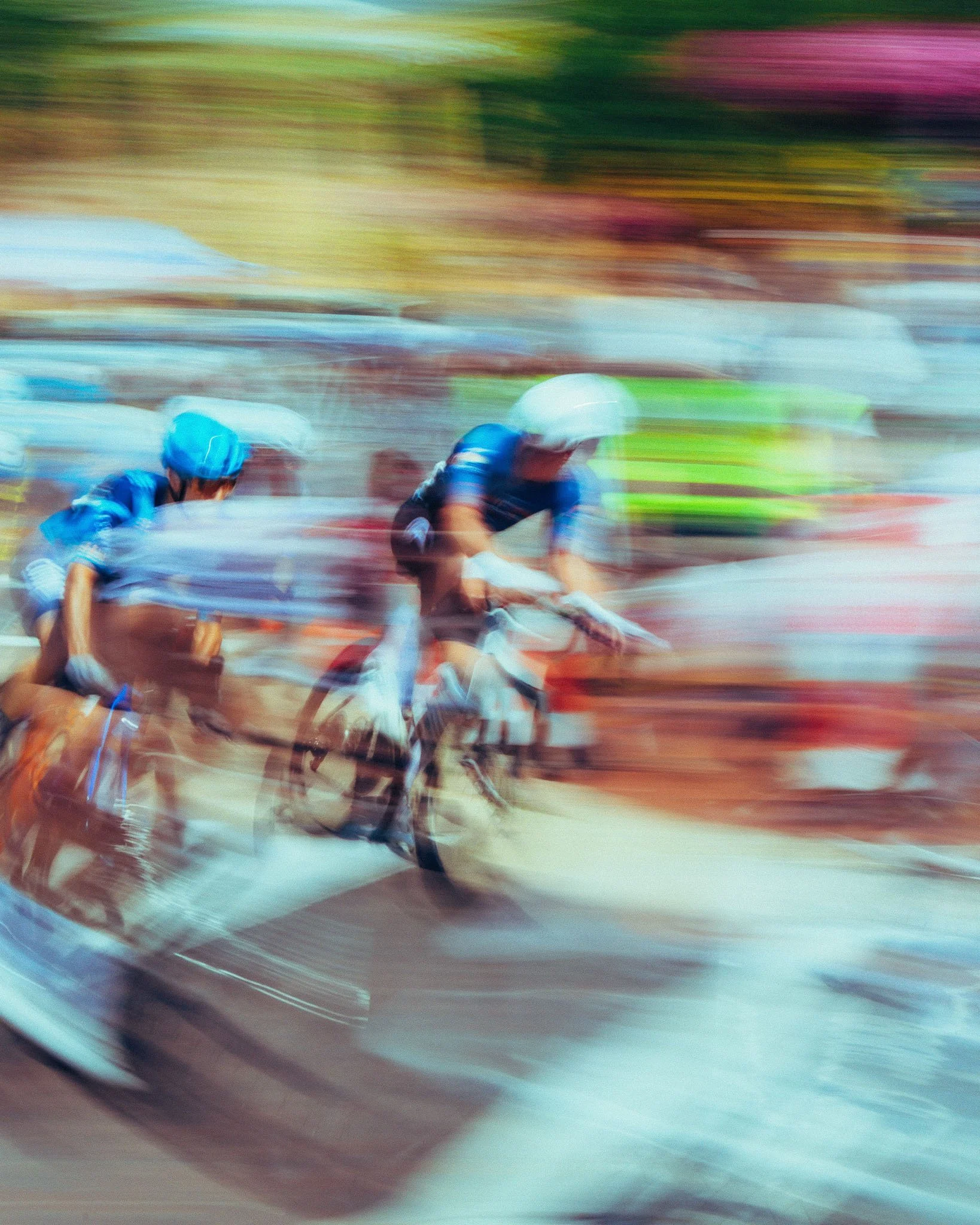 Blurred image of cyclists wearing helmets and racing gear, with an abstract background suggesting motion and speed.