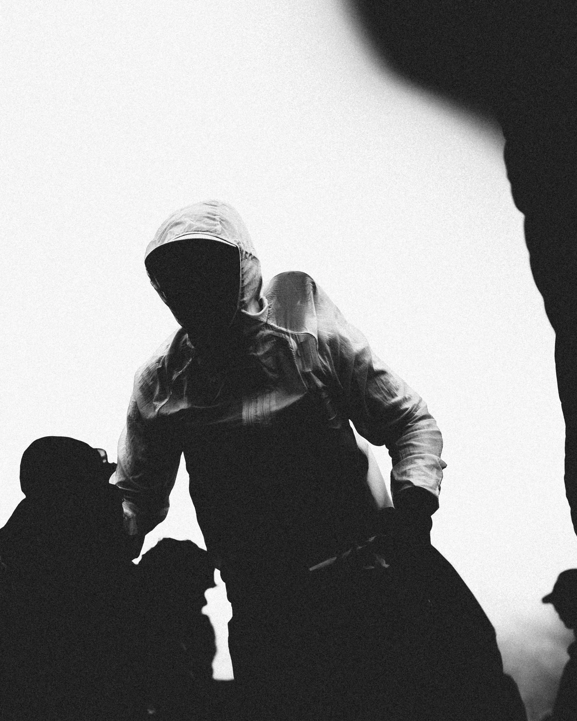 Four people are dabbing in a group silhouette against a plain light background, with their heads bowed and arms raised, creating a shadowy effect.
