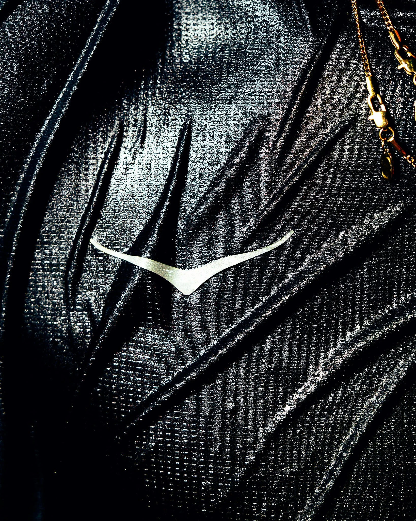 Close-up of Batman logo on black fabric with small reflective dots and part of a chain necklace.