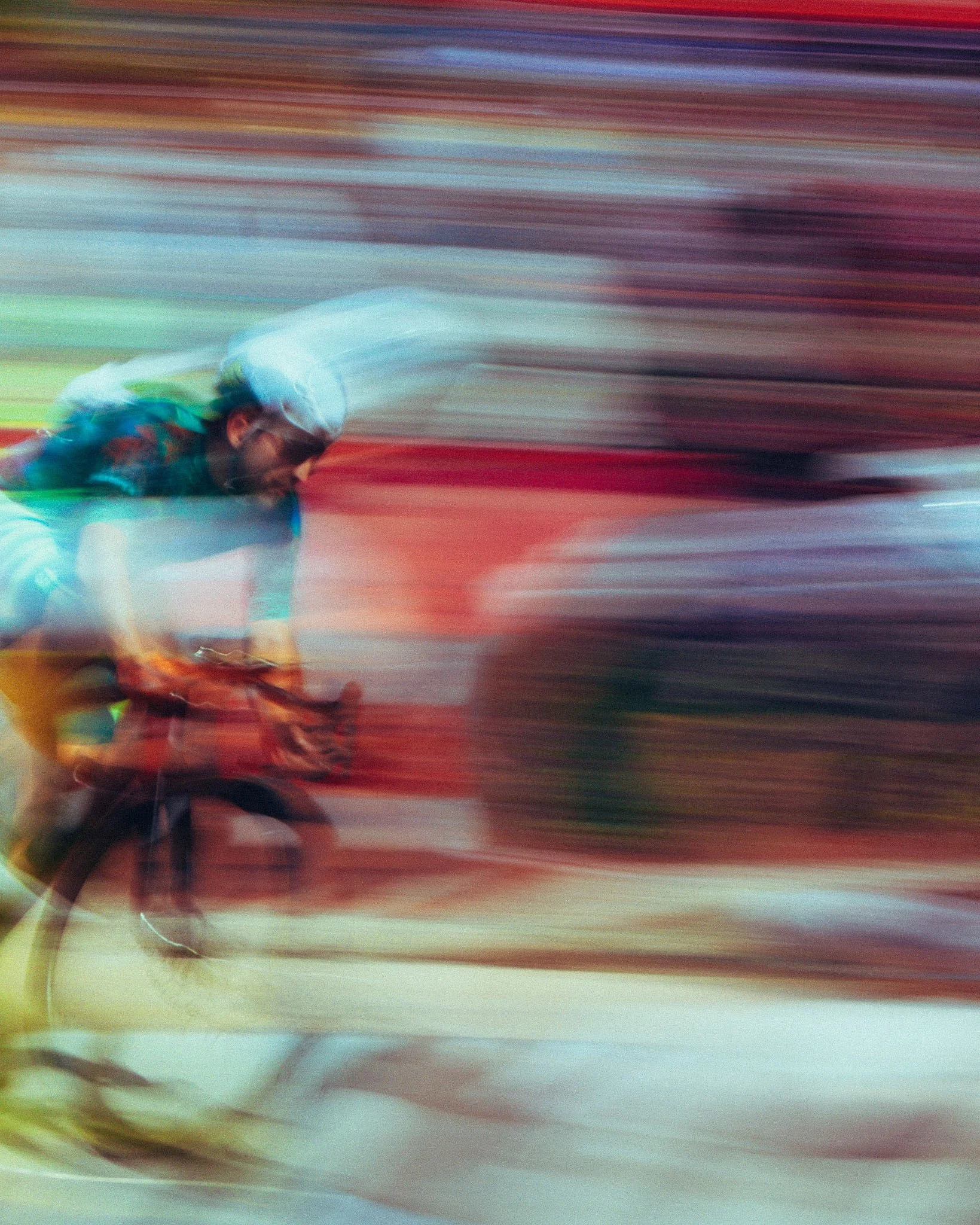A blurred photograph of a cyclist in a race, wearing a helmet and sunglasses, with colorful motion streaks in the background.
