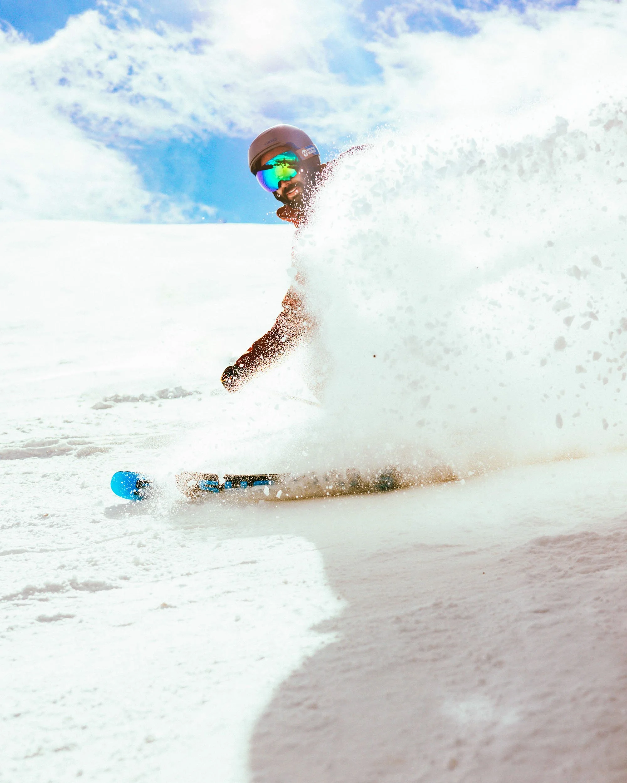 A skier wearing a helmet and sunglasses skis through fresh snow on a clear, sunny day.