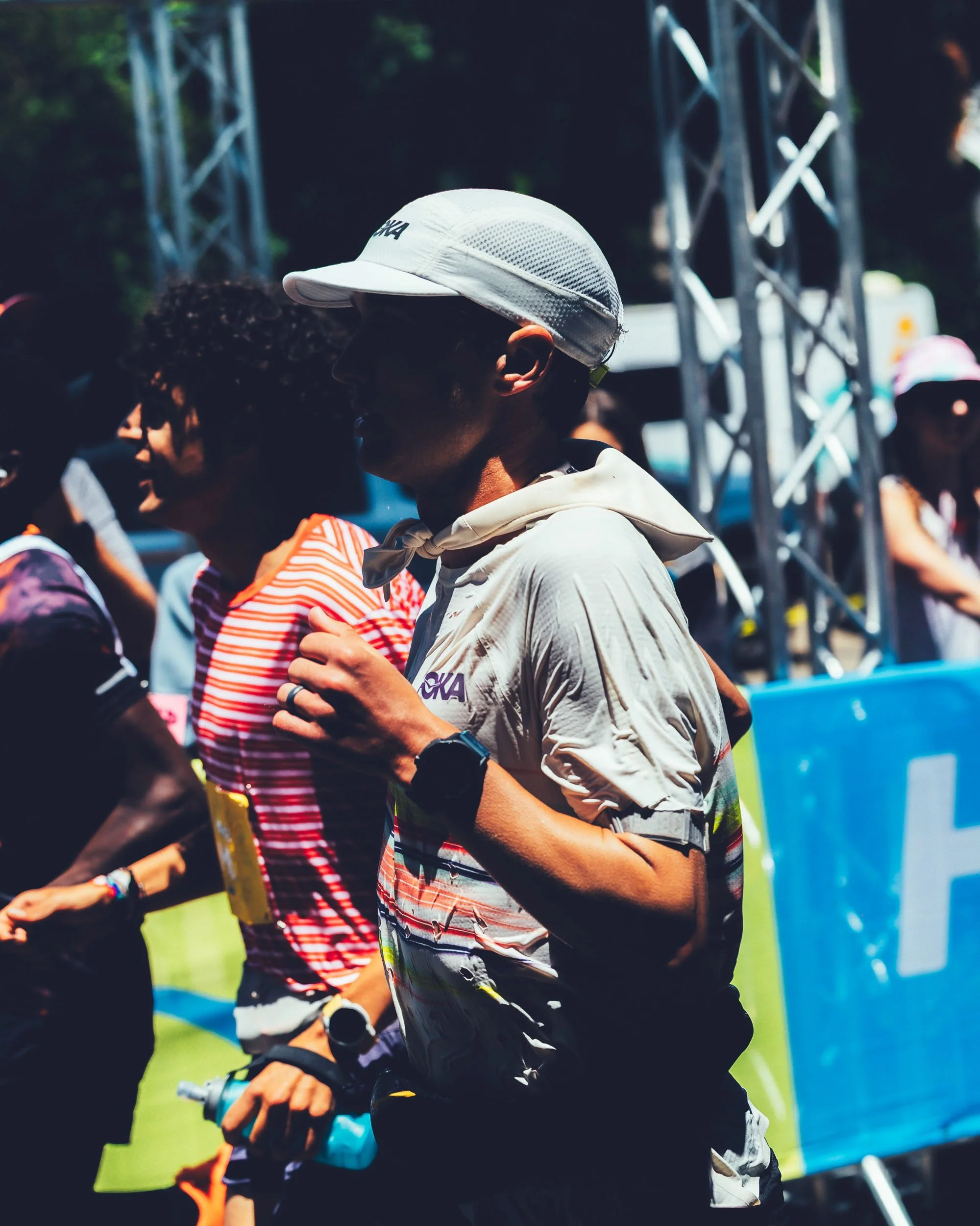 People participating in an outdoor event, some are wearing hats and sunglasses, with a structure in the background, possibly at a park or festival.