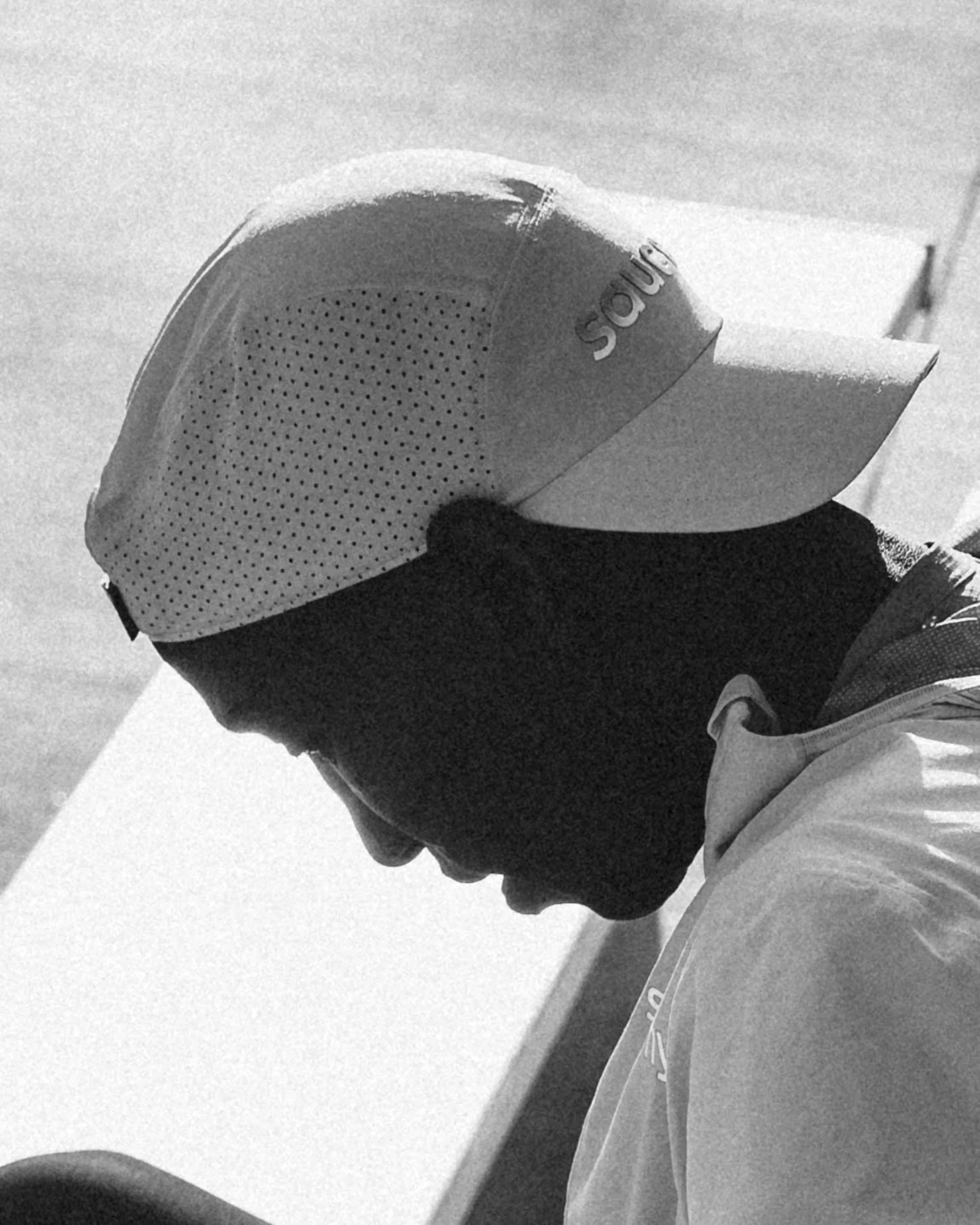 Close-up of a person in a sports jersey and cap, lowering their head with a background of clouded sky.