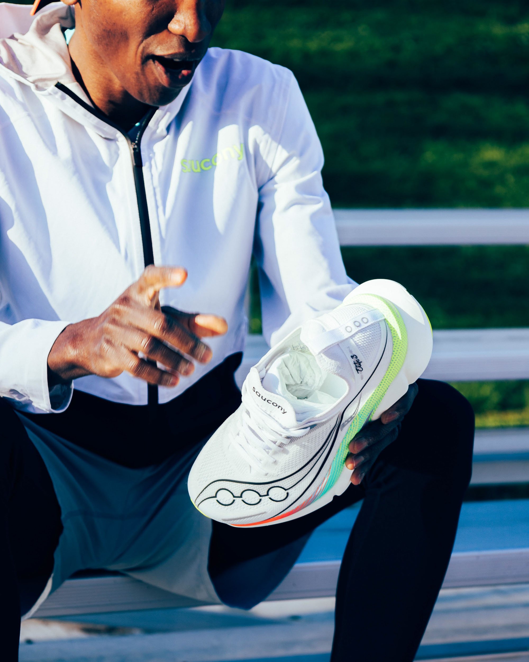 Close-up of a male athlete tying his running shoe during a track and field event, wearing a white sports jacket.