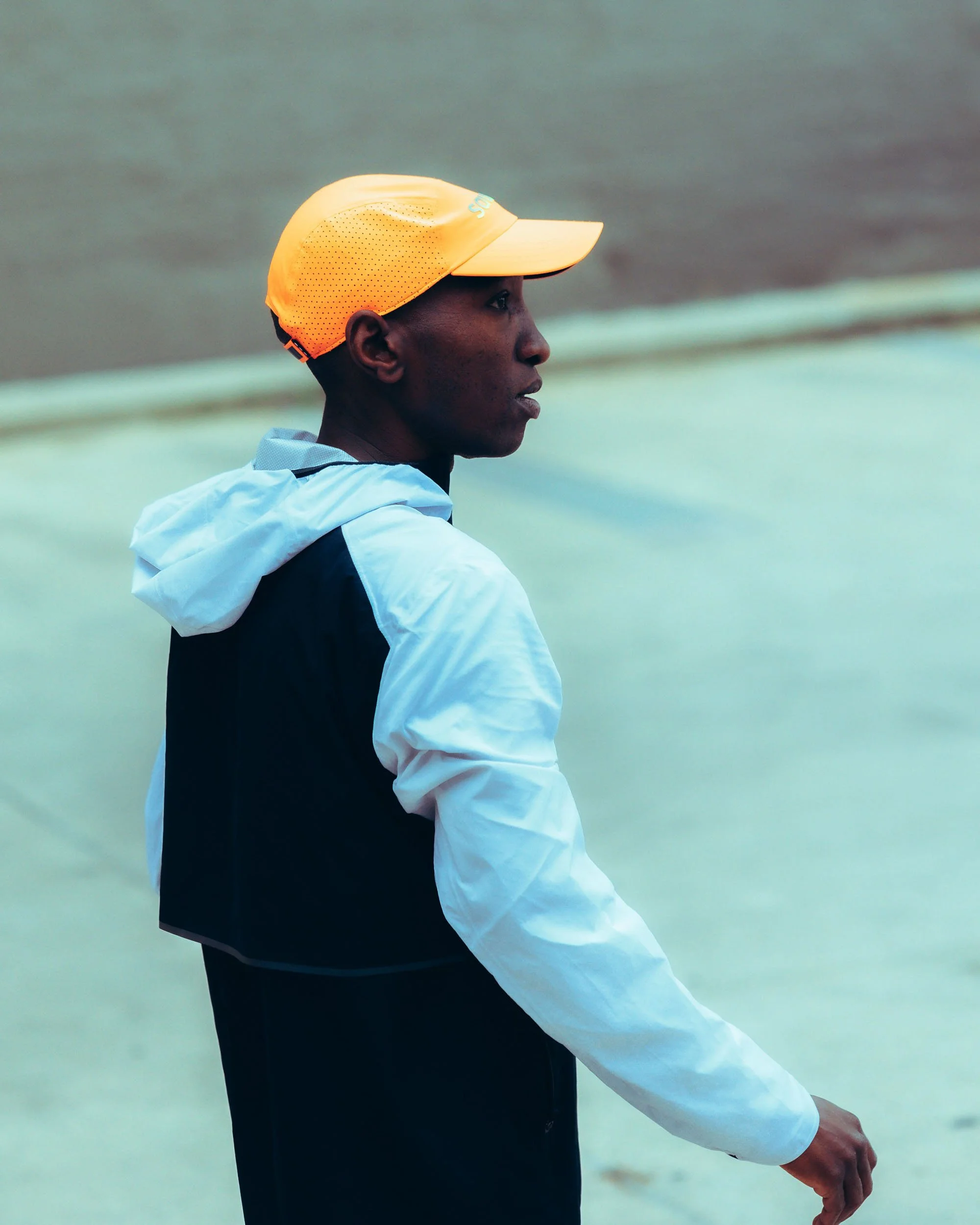 Close-up of a young man wearing a yellow cap and a white jacket, standing by the water.