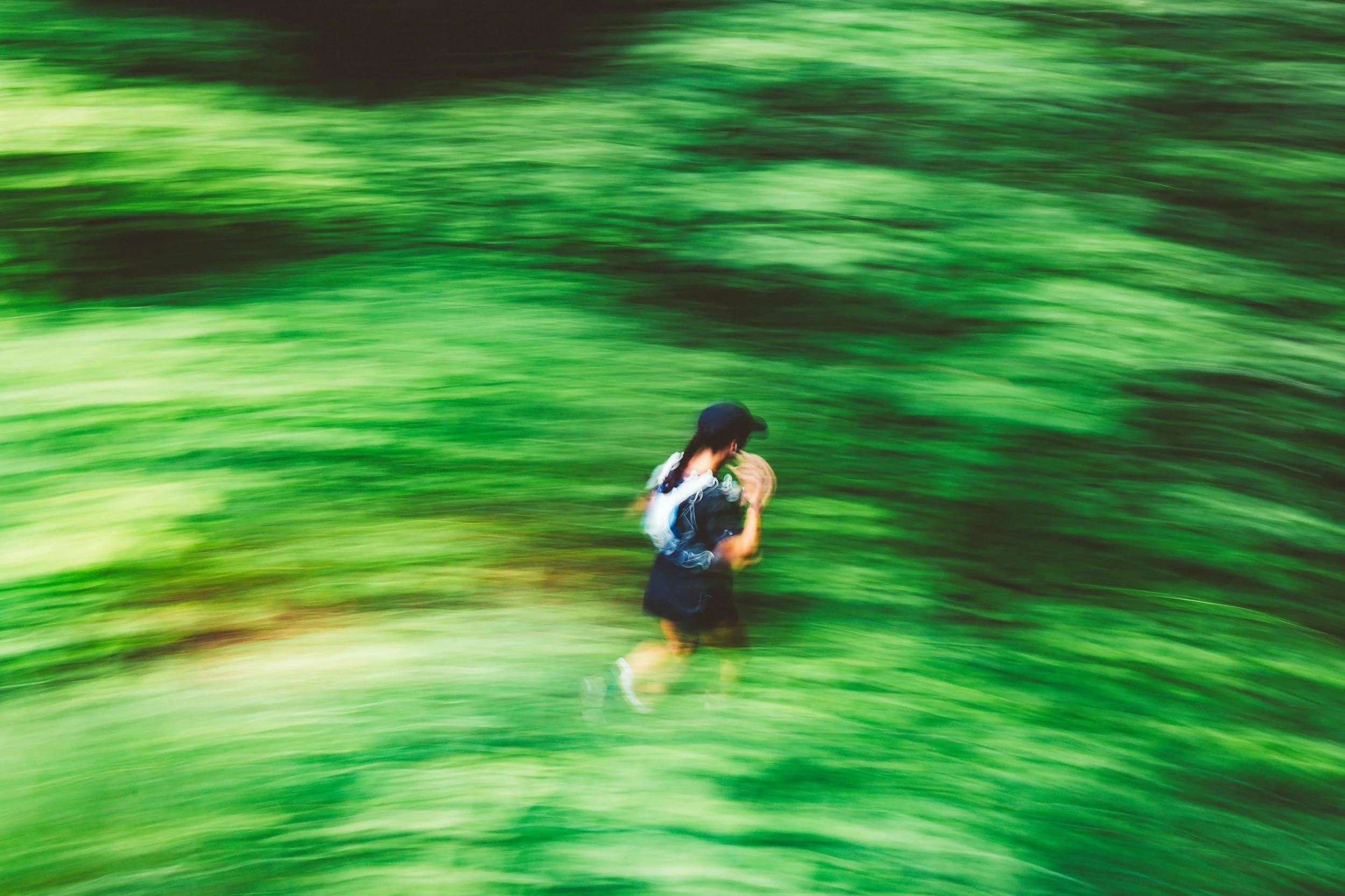 A person running through a lush green forest, blurred to convey motion.