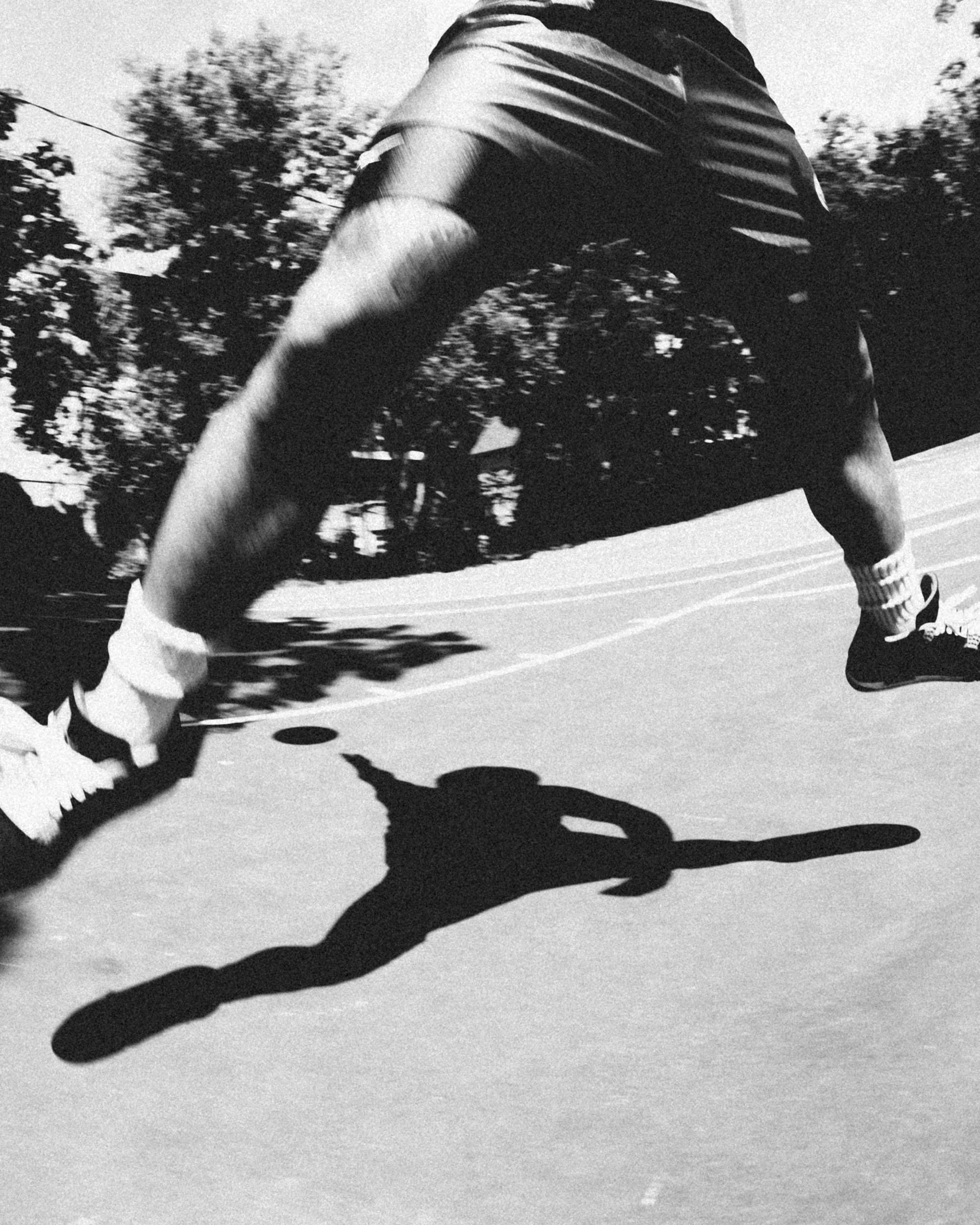 A person roller skating outdoors on a rink, casting a long shadow on the ice or pavement.