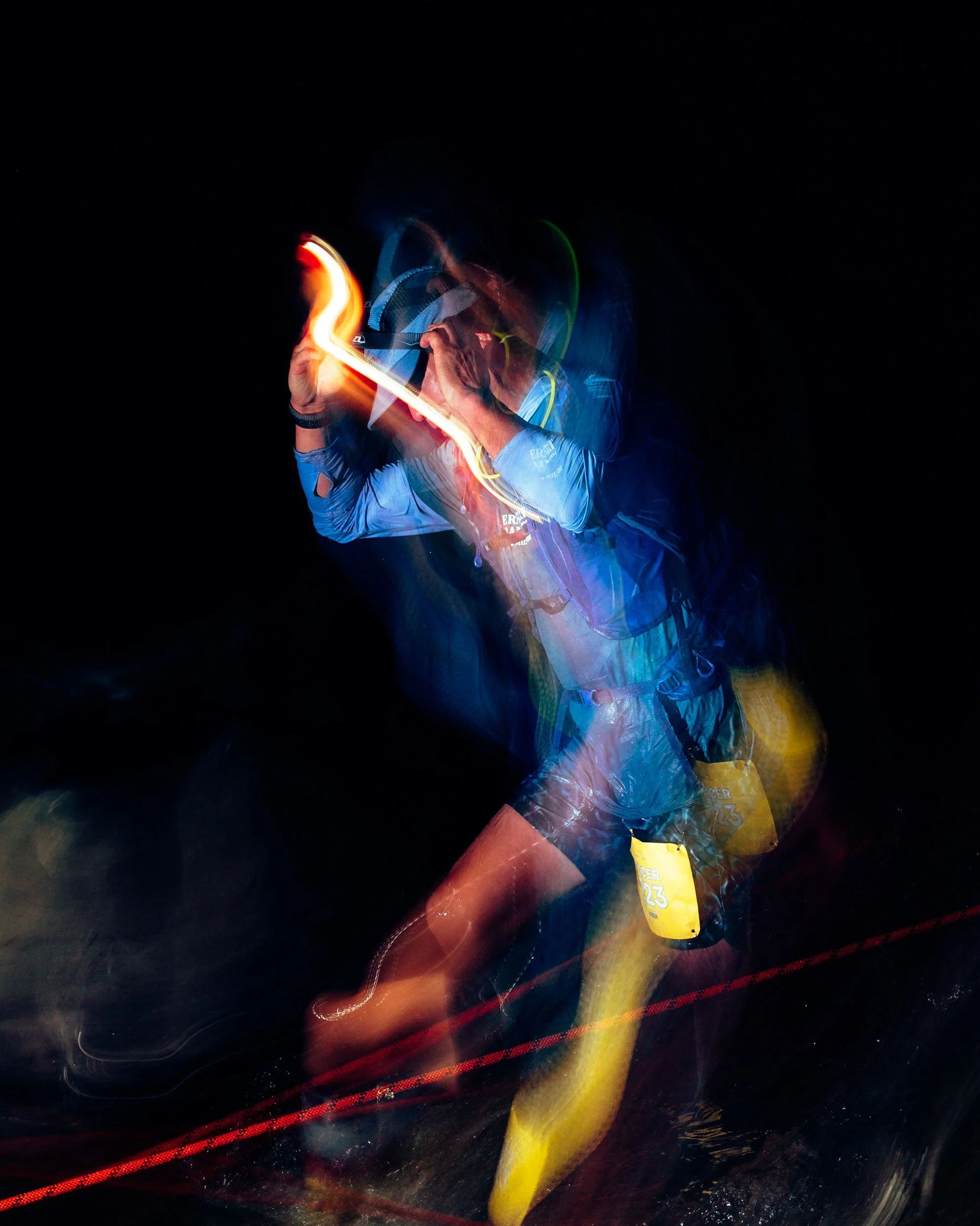 Person wearing a blue sports outfit with a yellow tag, holding a light stick or glow stick, during a night event, surrounded by light trails and darkness.