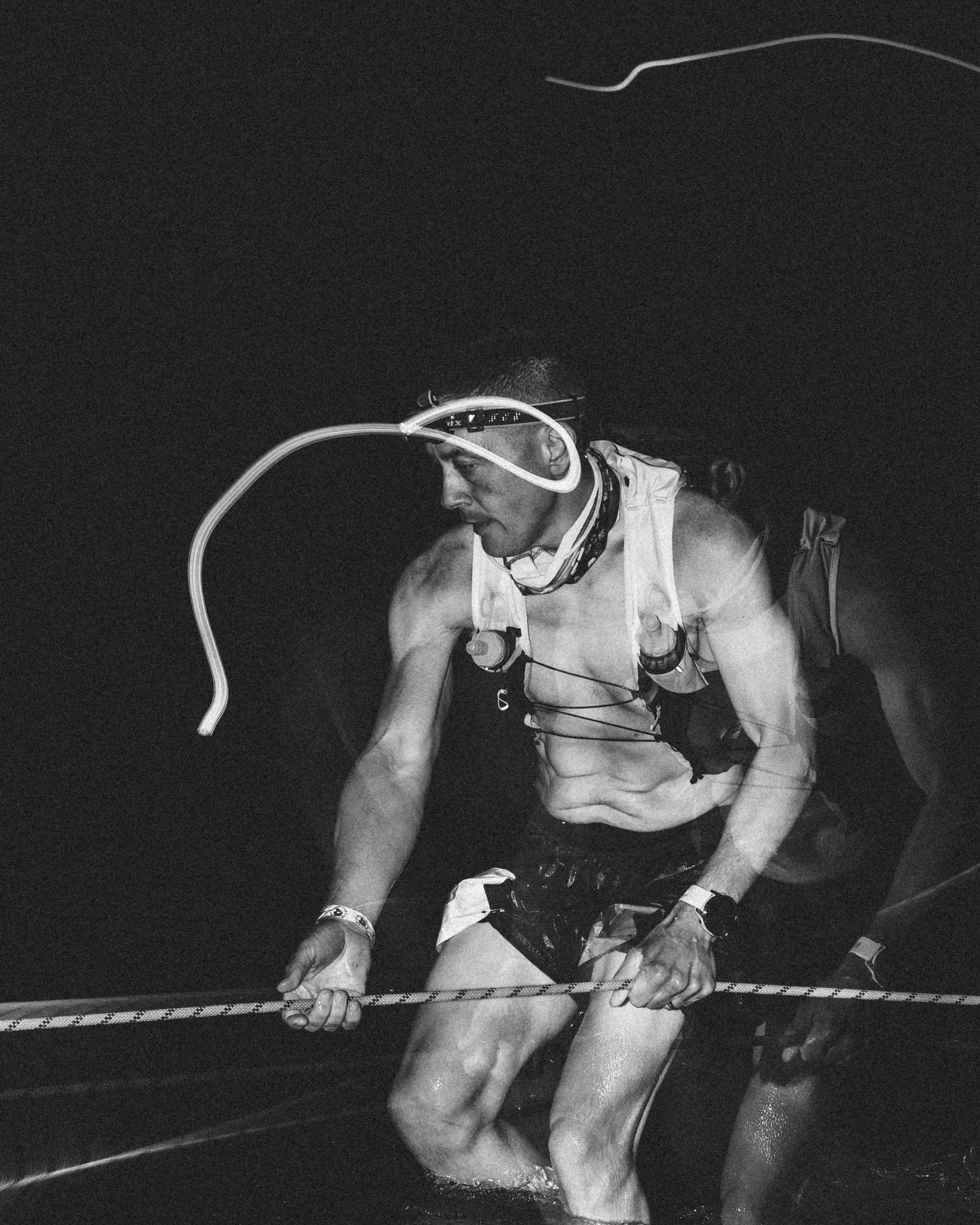 A male athlete is in water, wearing a breathing apparatus with a mask and tubes, and holding a rope or cord, appearing to be in a training or competitive environment.