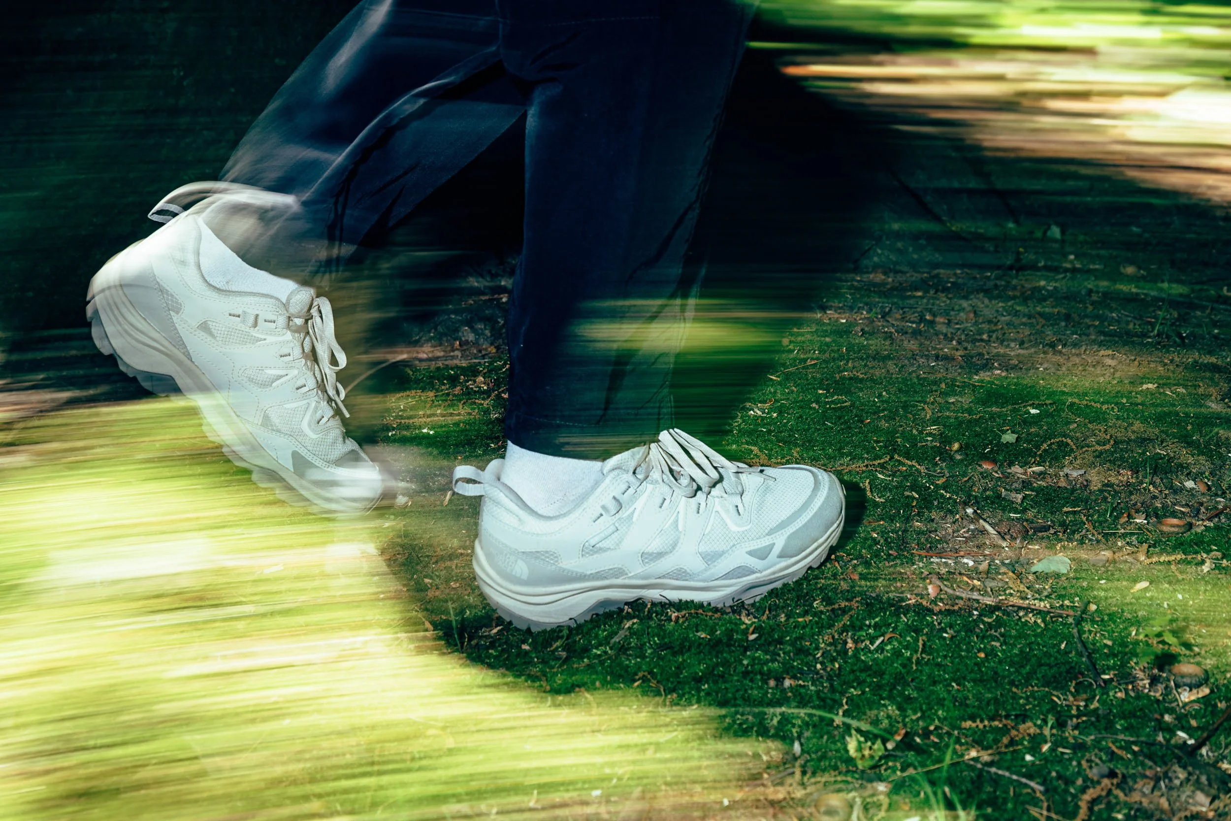 Close-up of white athletic shoes on a person's feet as they walk on a mossy, forest ground with motion blur effect.