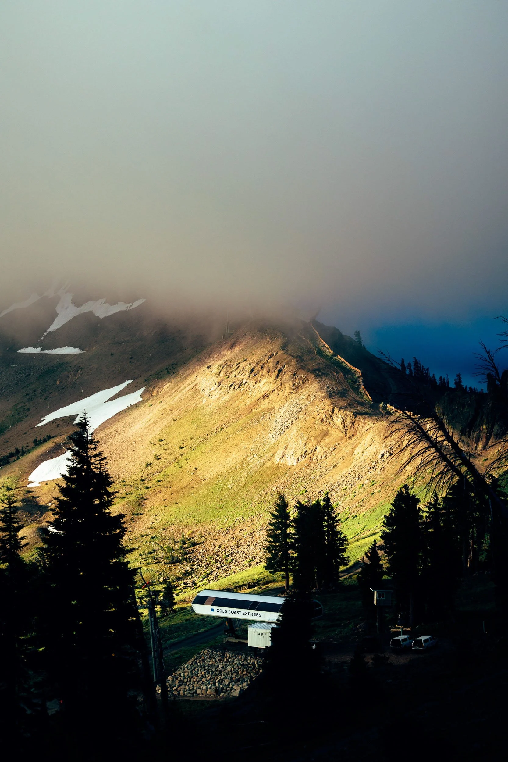 Scenic mountain landscape with trees in foreground, partly snowy slopes, and a cable car labeled 'GOLD COAST EXPRESS' near a small building at the base.