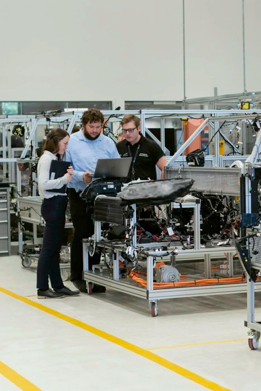 Three engineers examining machinery and electronics on a worktable in a manufacturing or testing facility.