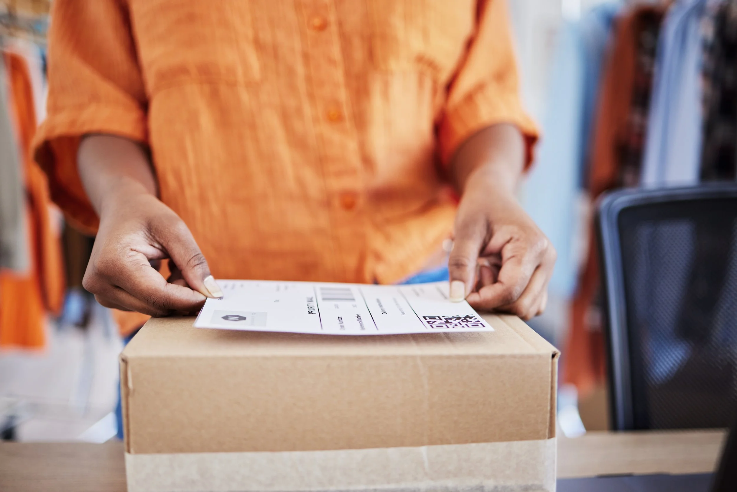 Person in orange shirt attaching a shipping label to a cardboard box.